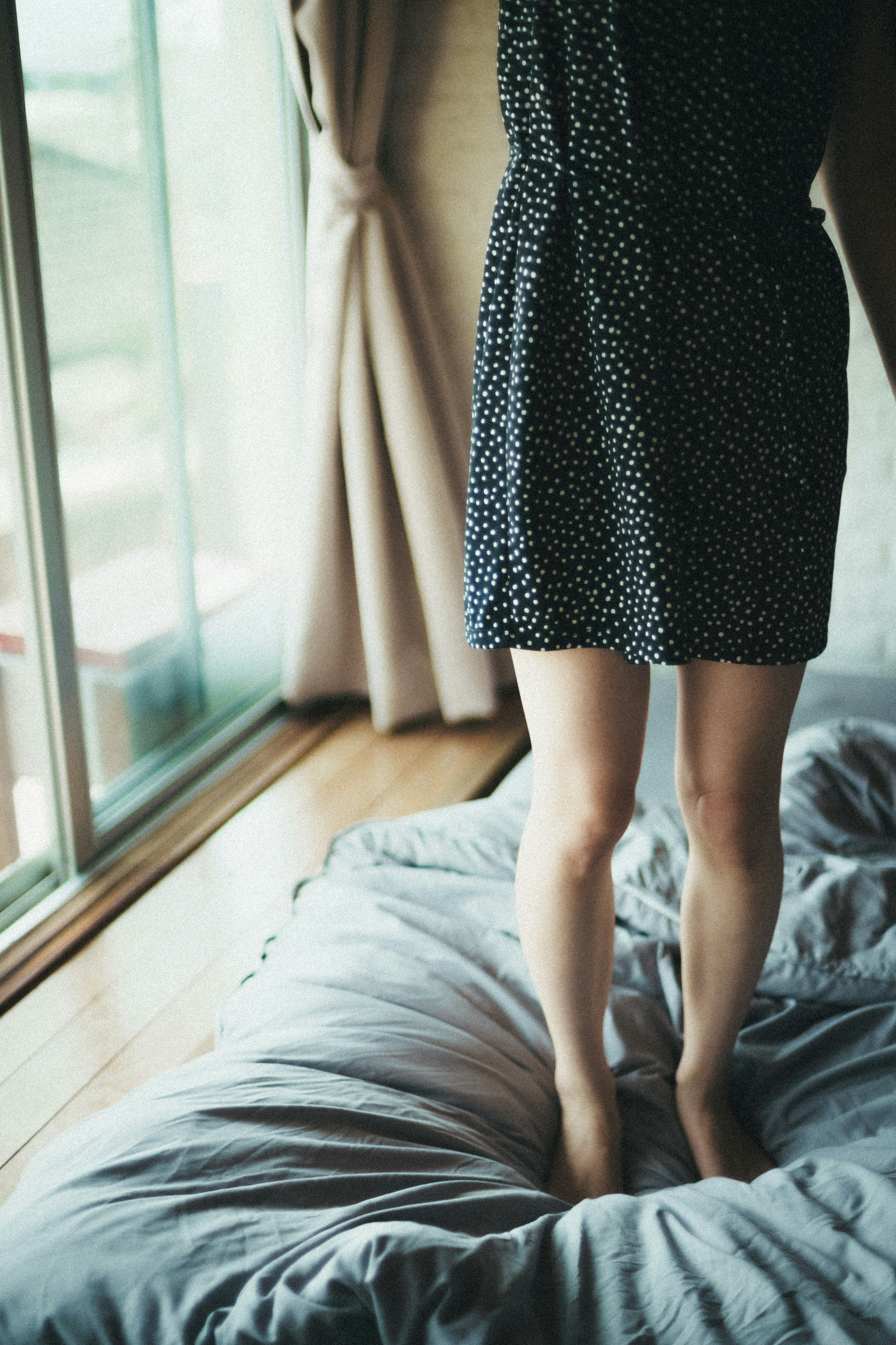 Füße einer Frau, die an einem Fenster in einem gepunkteten Kleid steht