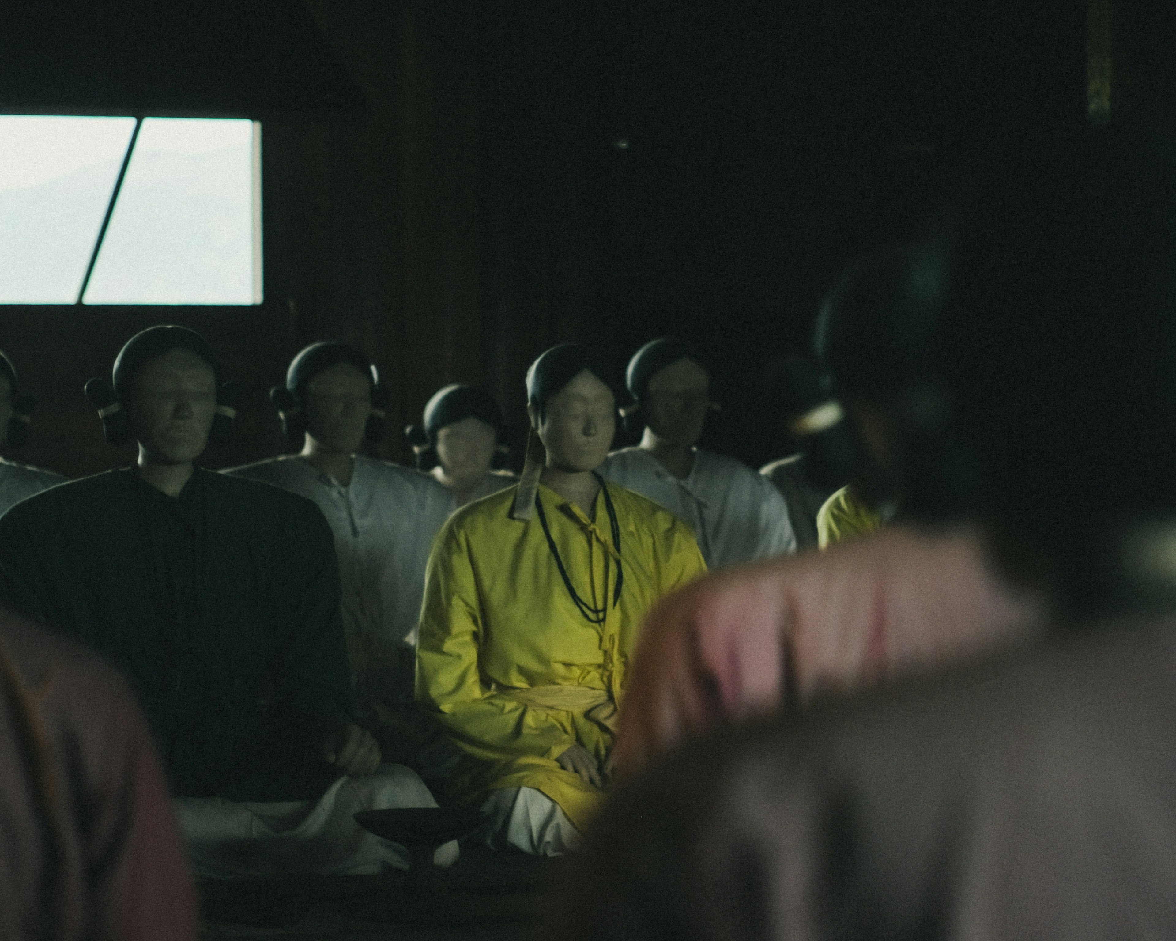 Group of individuals seated in a dimly lit room with a prominent figure in yellow clothing