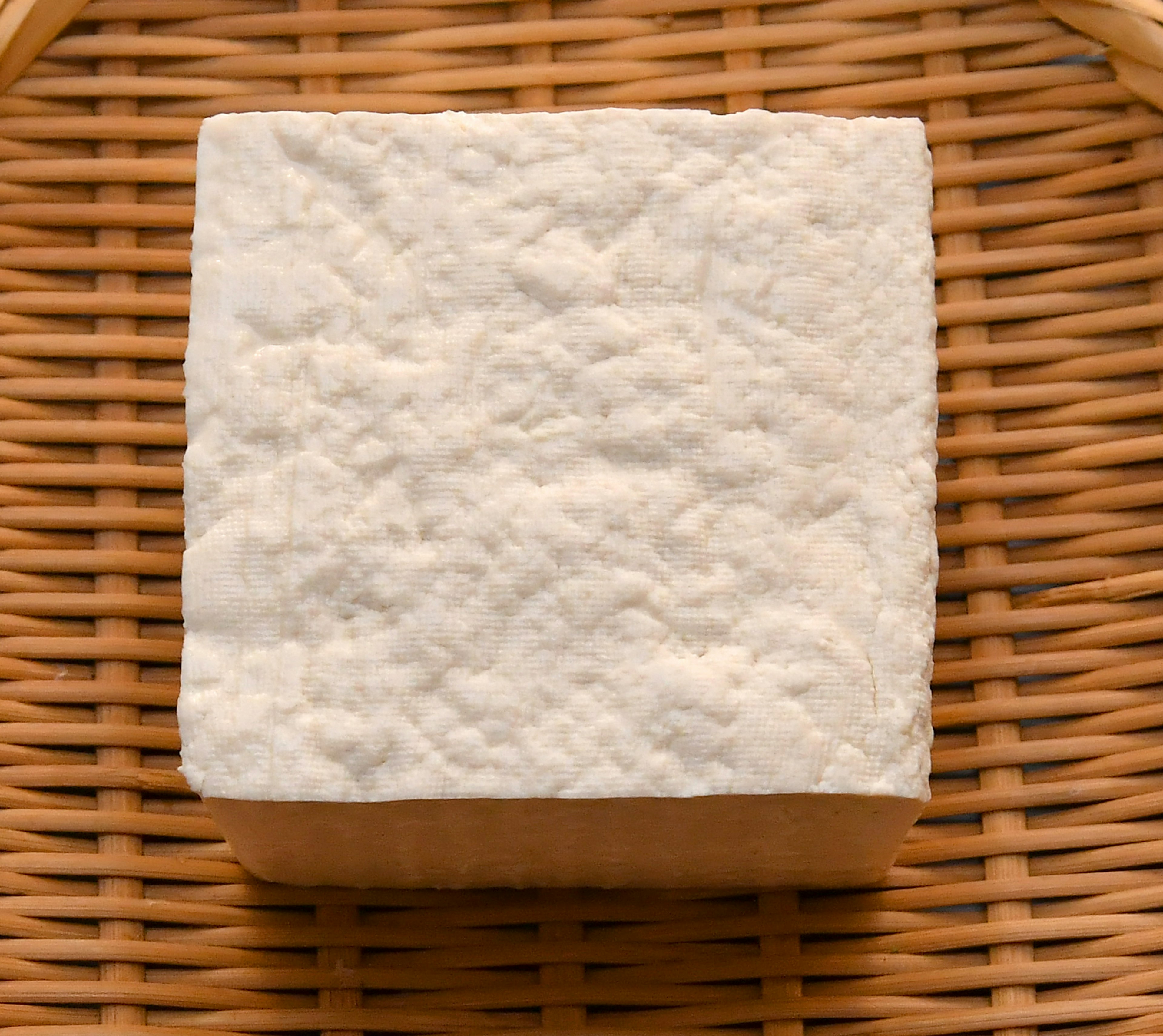 Tofu blanc en forme de carré posé sur un panier en bambou