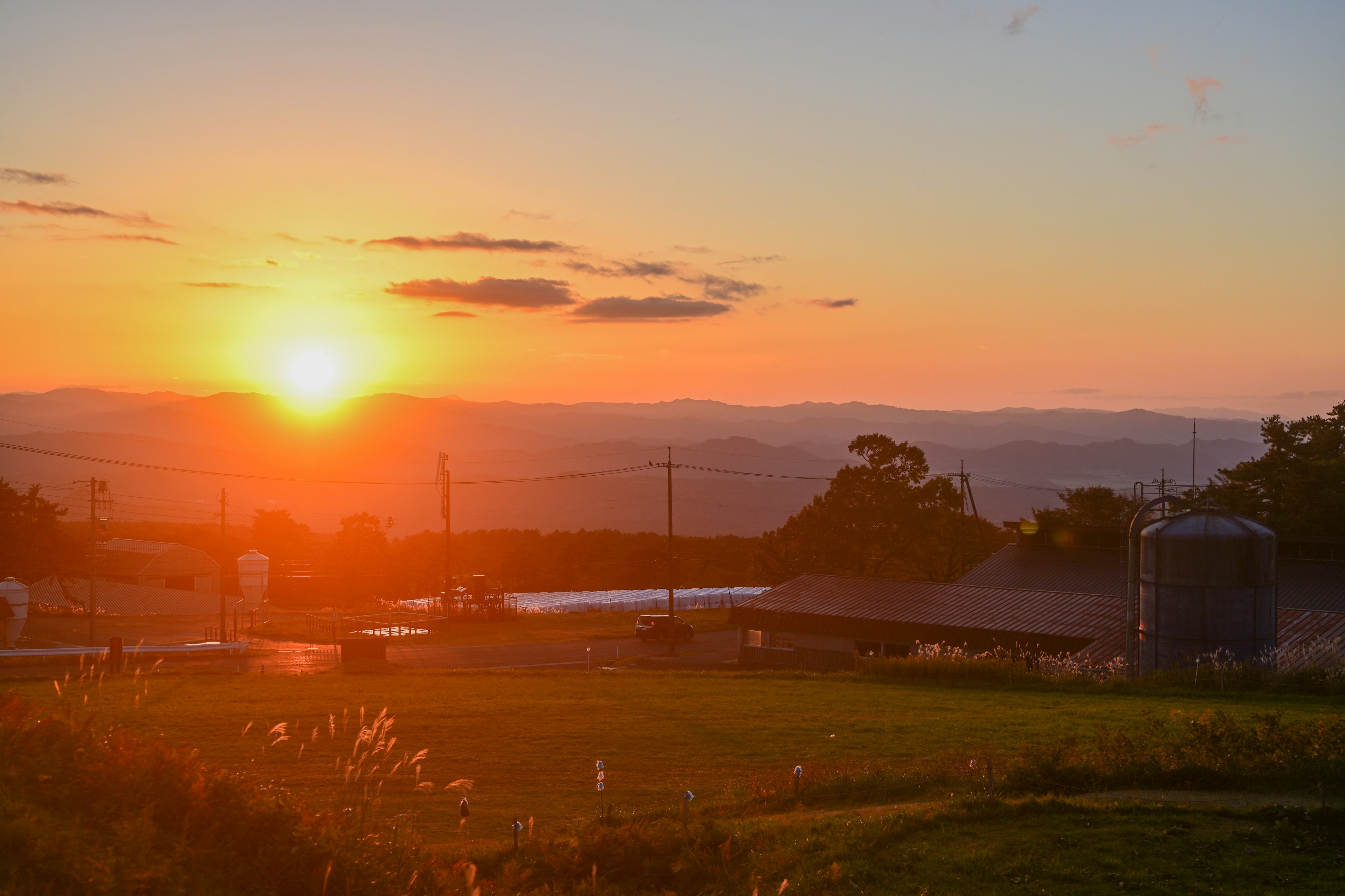 Una hermosa puesta de sol sobre colinas onduladas con una tranquila escena de granja