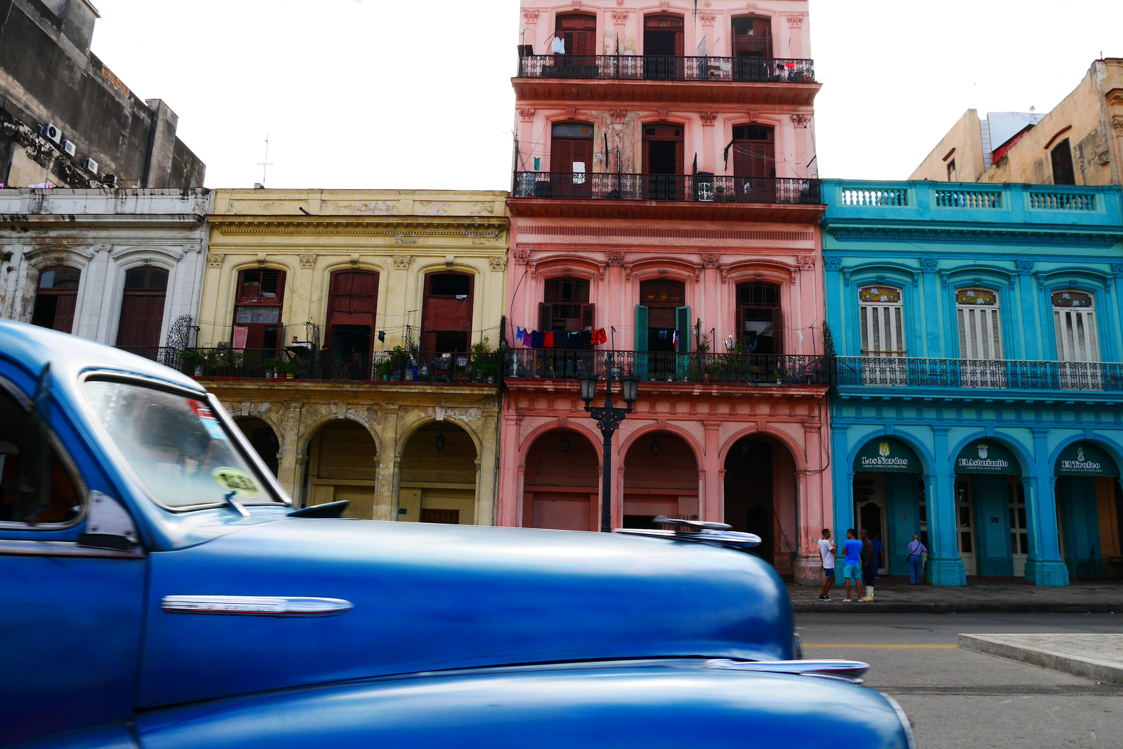 A blue vintage car in front of colorful colonial buildings