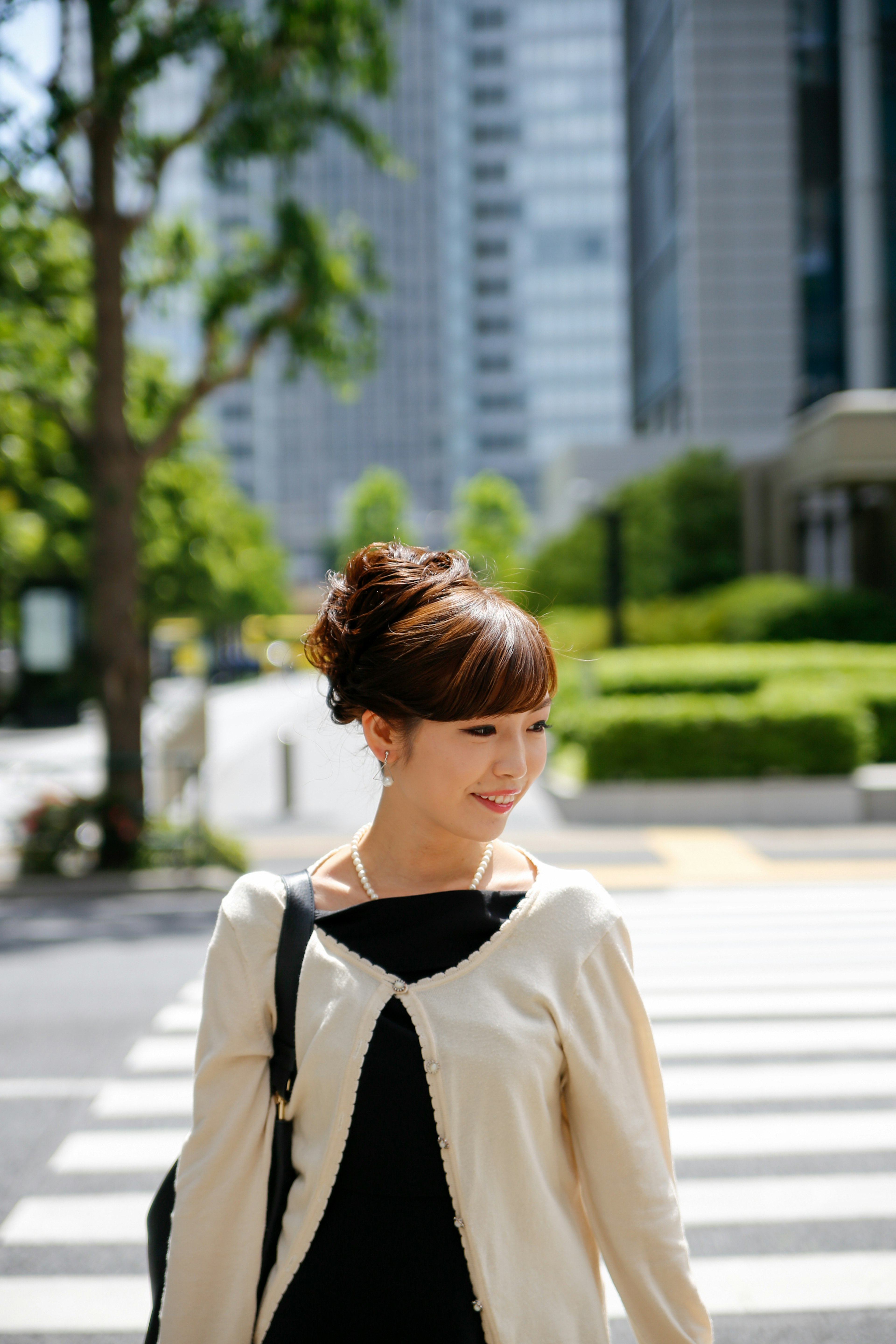 Woman walking on a city crosswalk with green trees and skyscrapers in the background