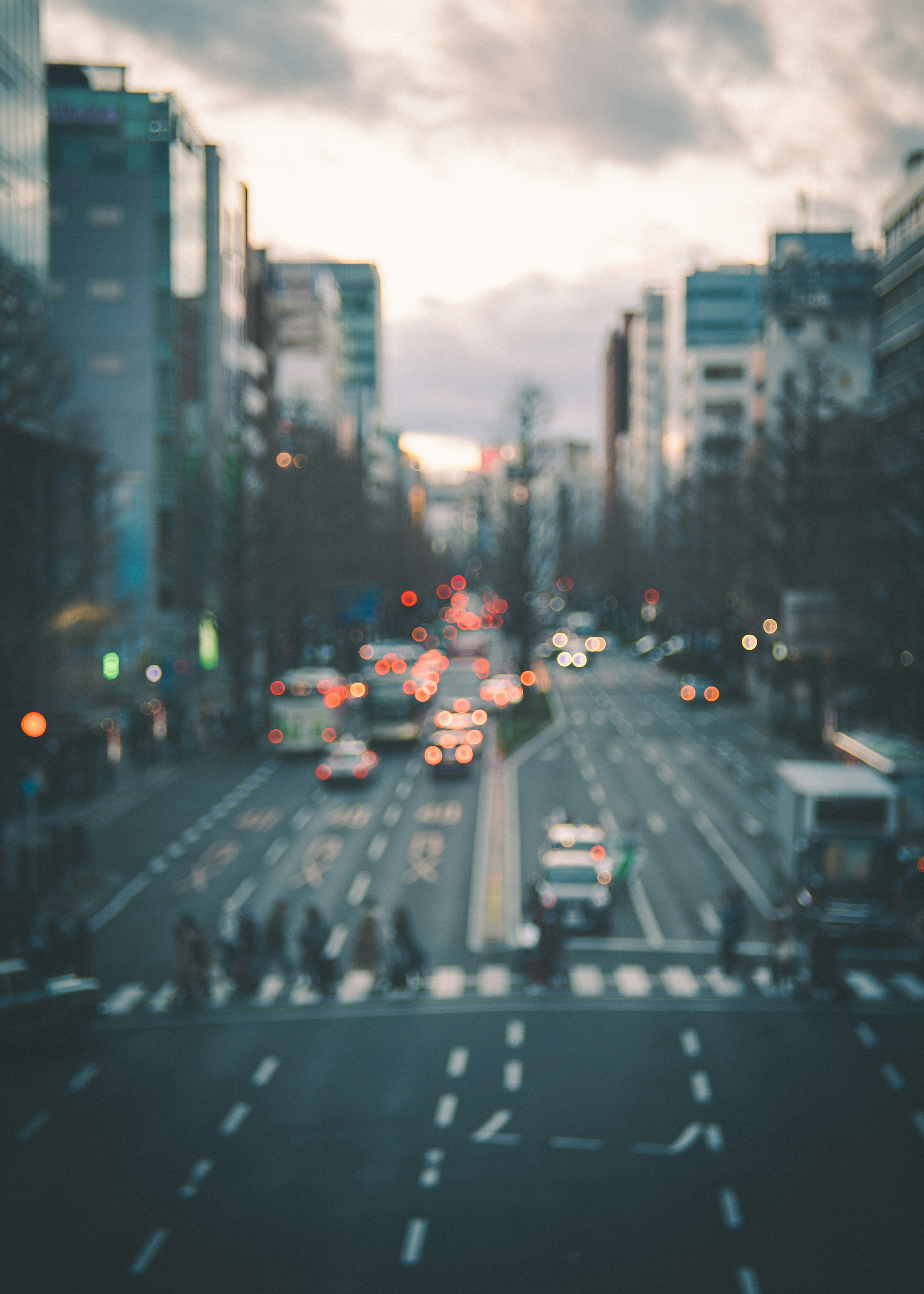 Foto borrosa de una calle de la ciudad y una intersección al atardecer con tráfico y peatones