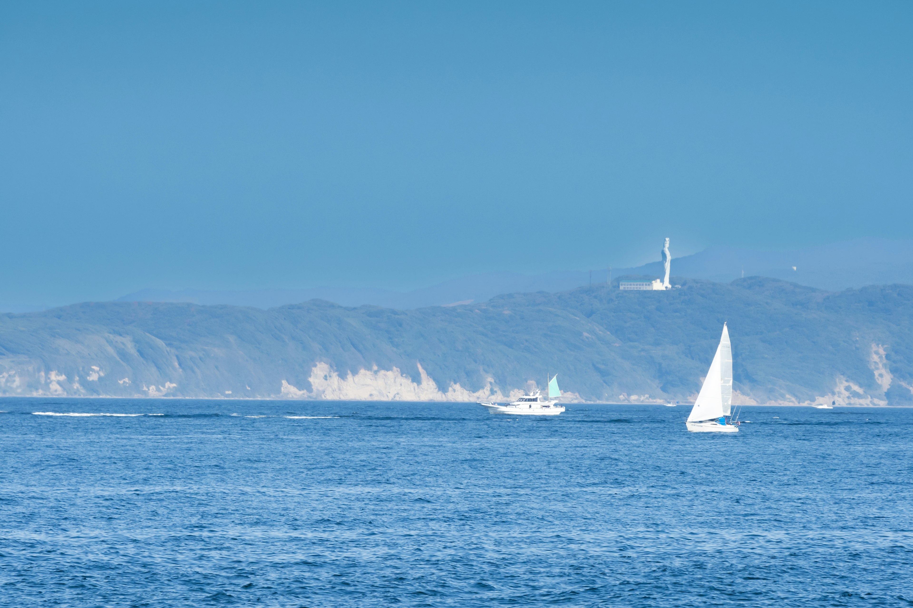 Velero y lancha en un mar azul con colinas distantes