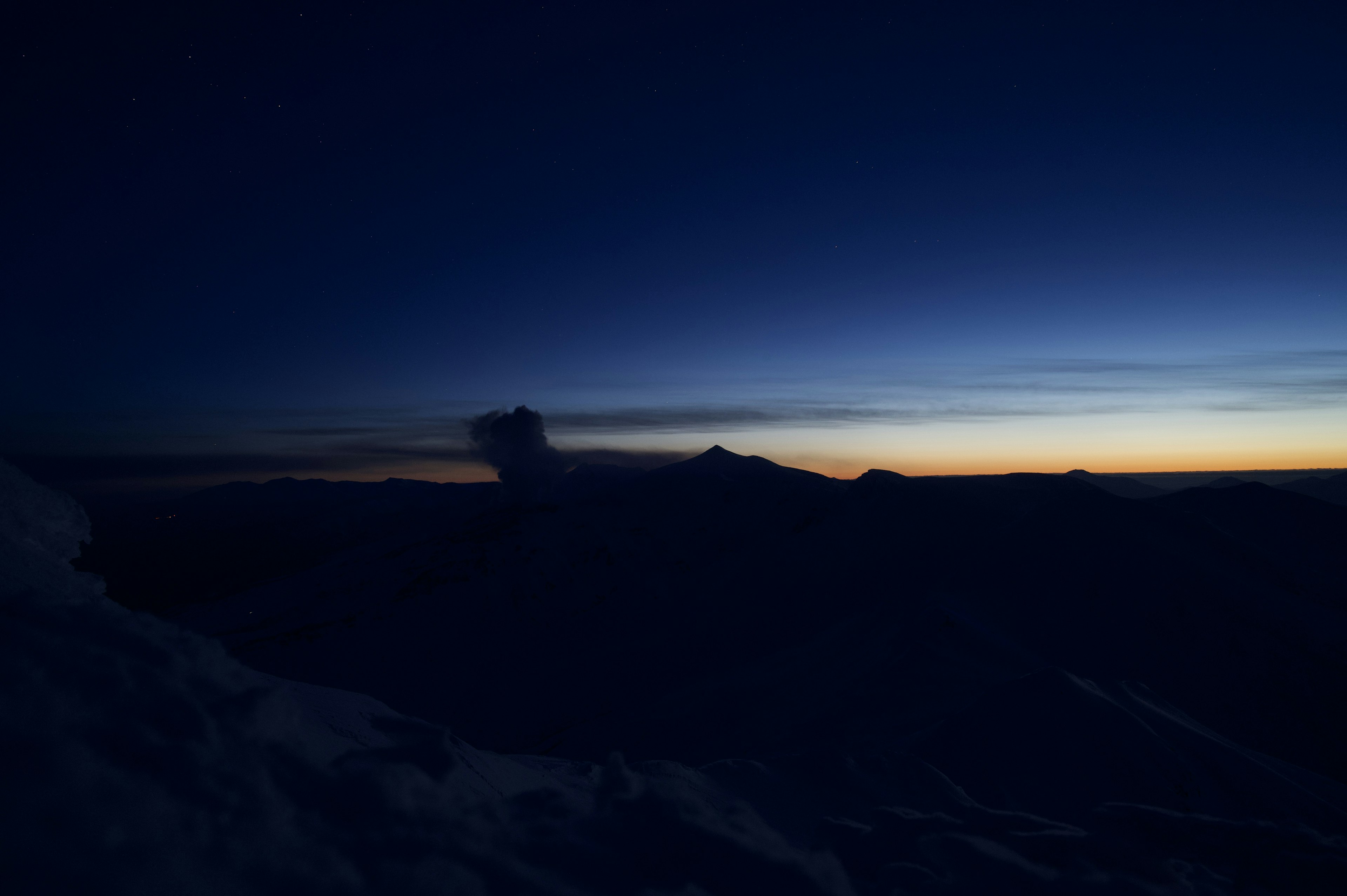 Silhouette von Bergen gegen einen Farbverlauf aus Blau und Orange im Nachthimmel