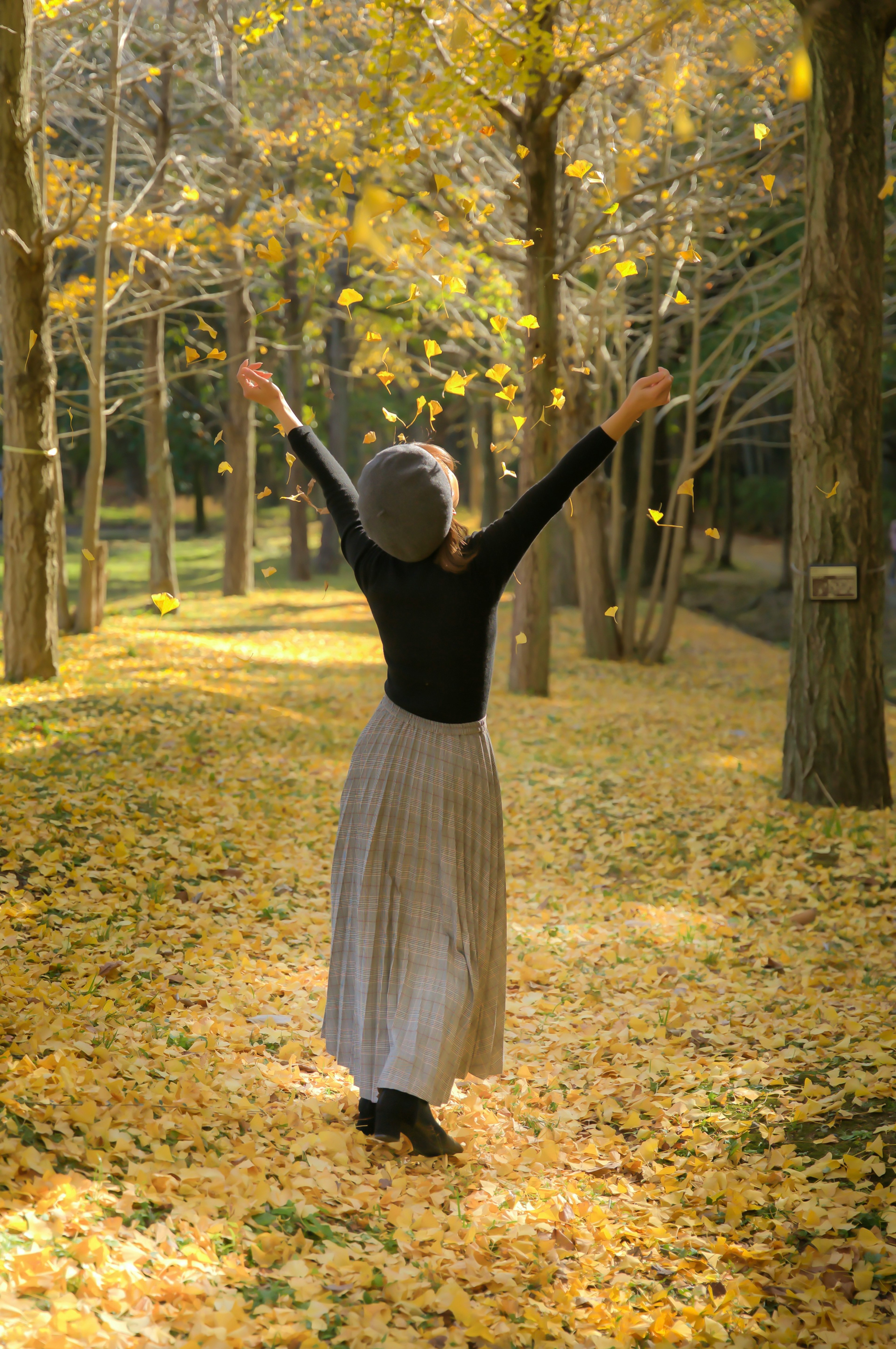 Frau mit erhobenen Armen auf einem herbstlichen Waldweg, bedeckt mit gelben Blättern