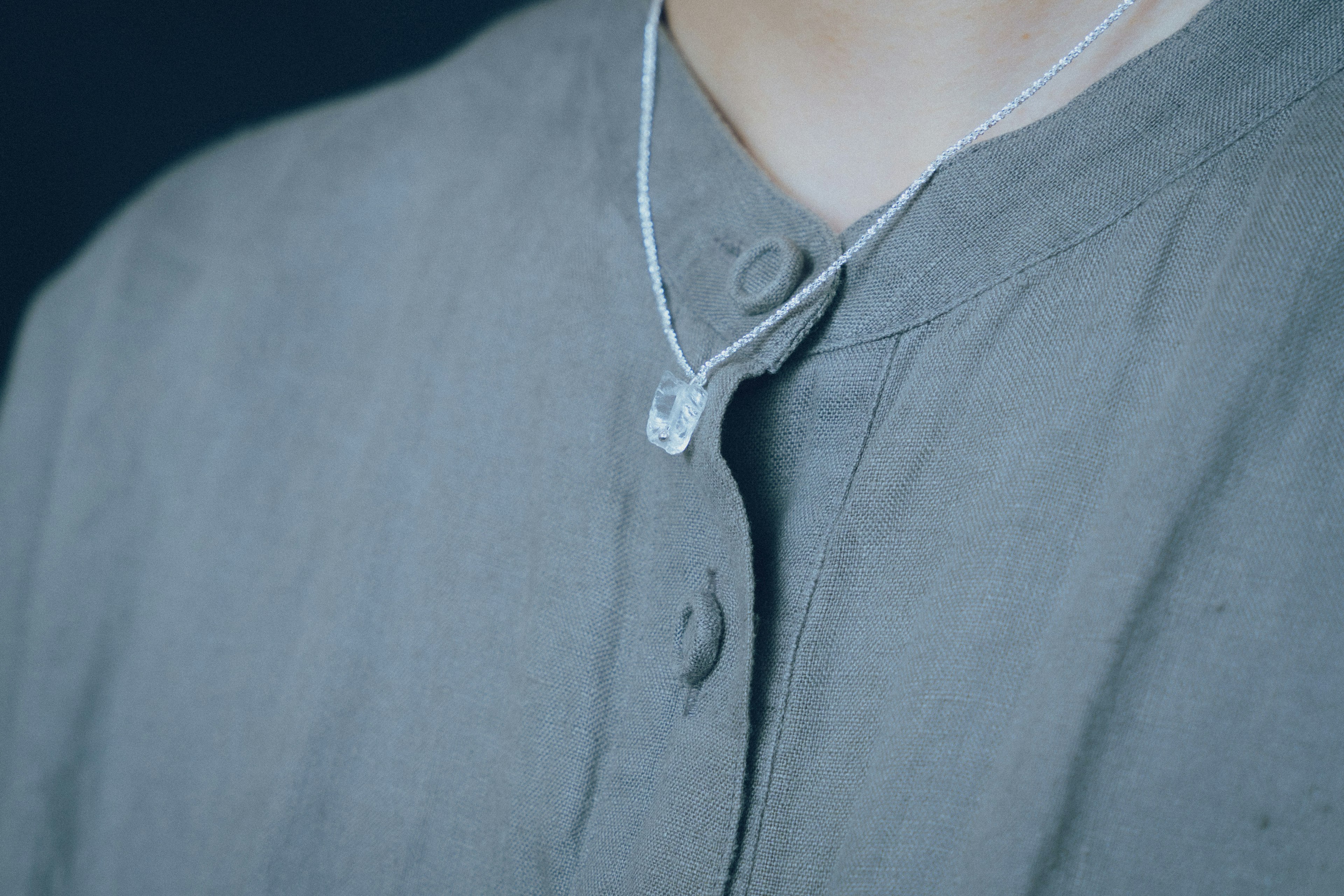 Une personne portant une chemise grise avec un pendentif transparent suspendu au cou