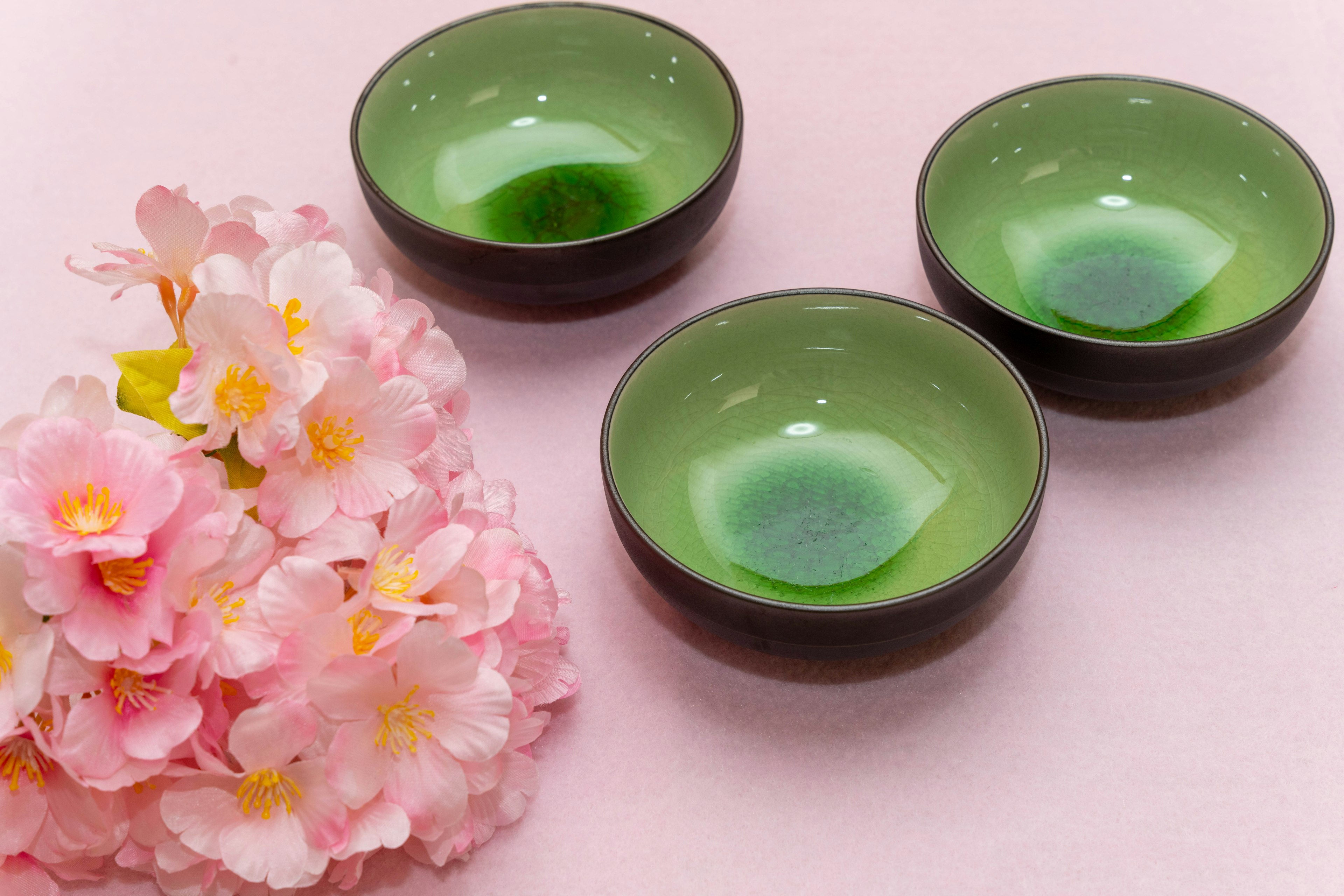 Three small green bowls arranged with pink flowers on a soft background