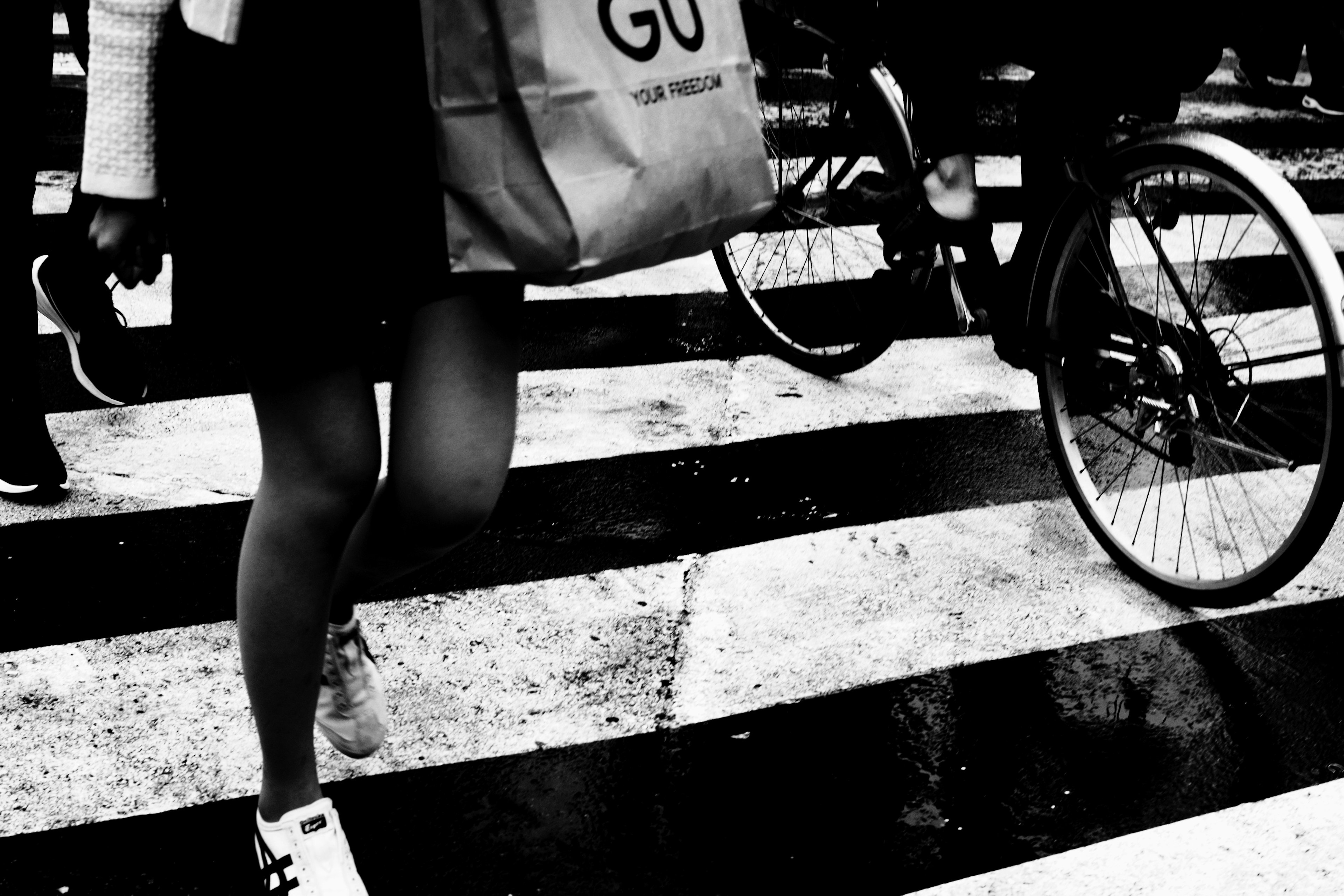 Una persona cruzando un paso de cebra con una bicicleta cerca llevando una bolsa de compras