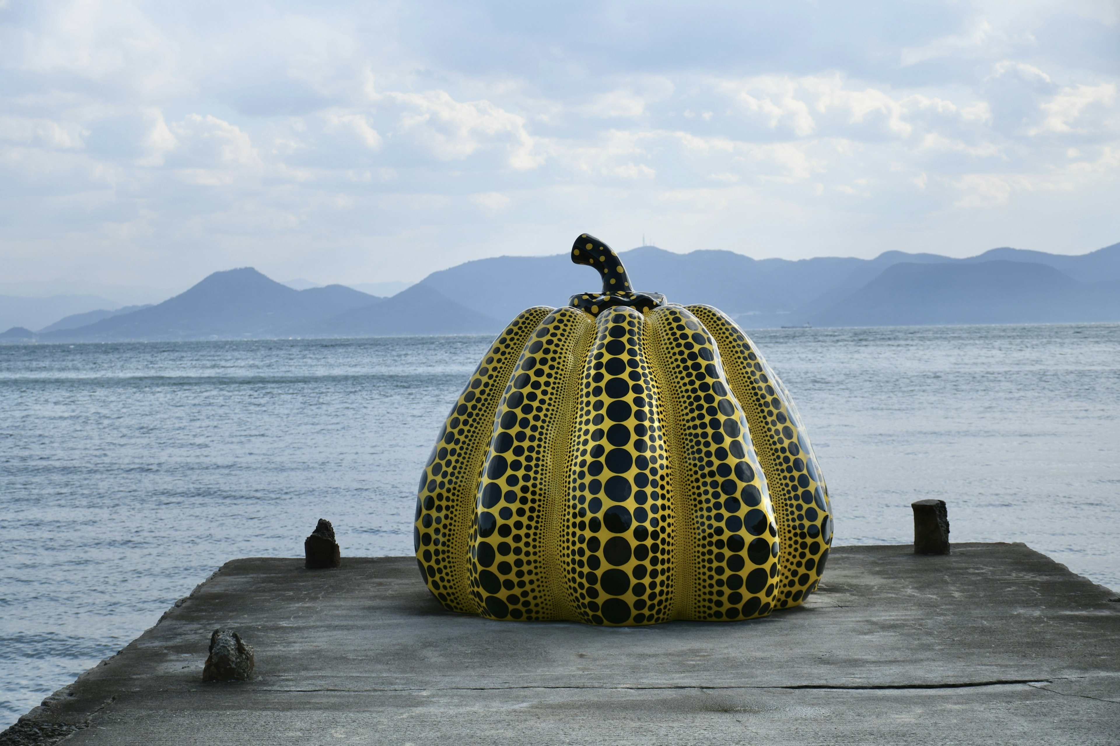 海に浮かぶ黄色のカボチャの彫刻と黒い水玉模様