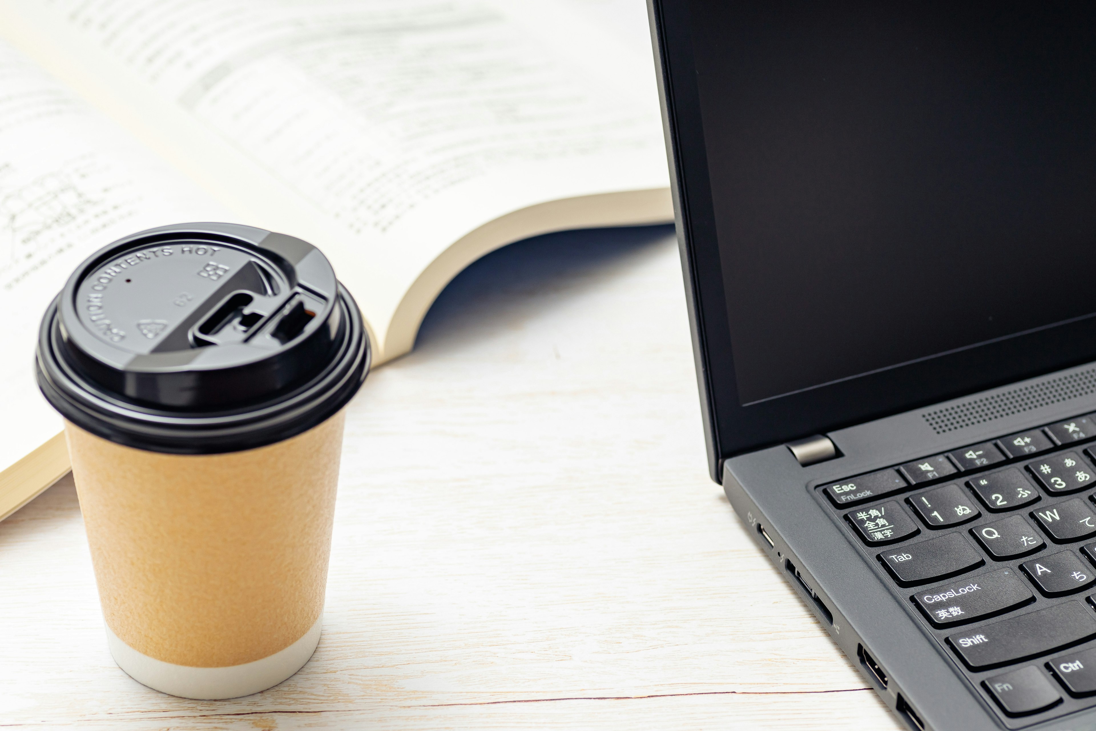 Coffee cup next to a laptop on a desk with an open book