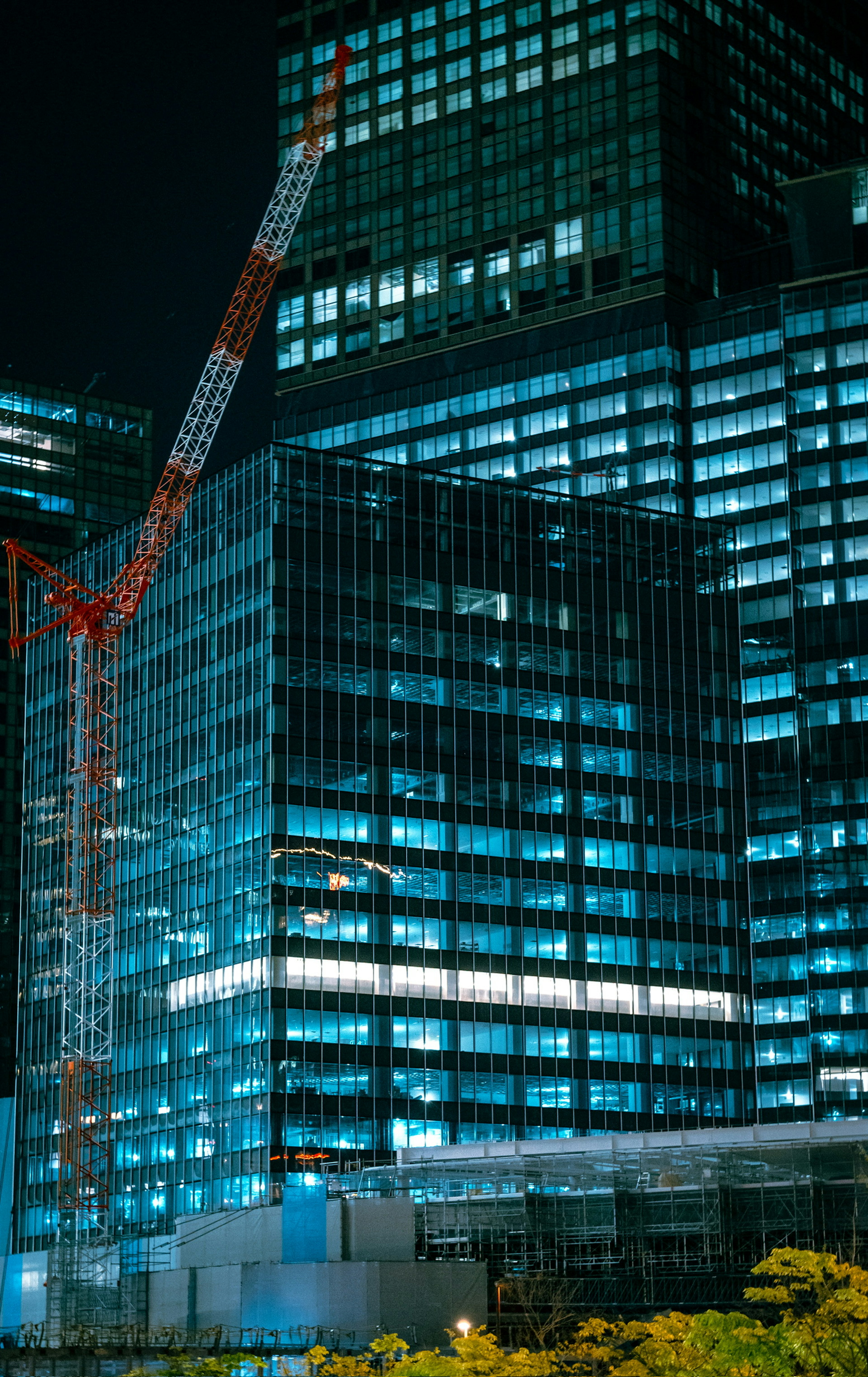 High-rise buildings illuminated in blue light at night with a crane