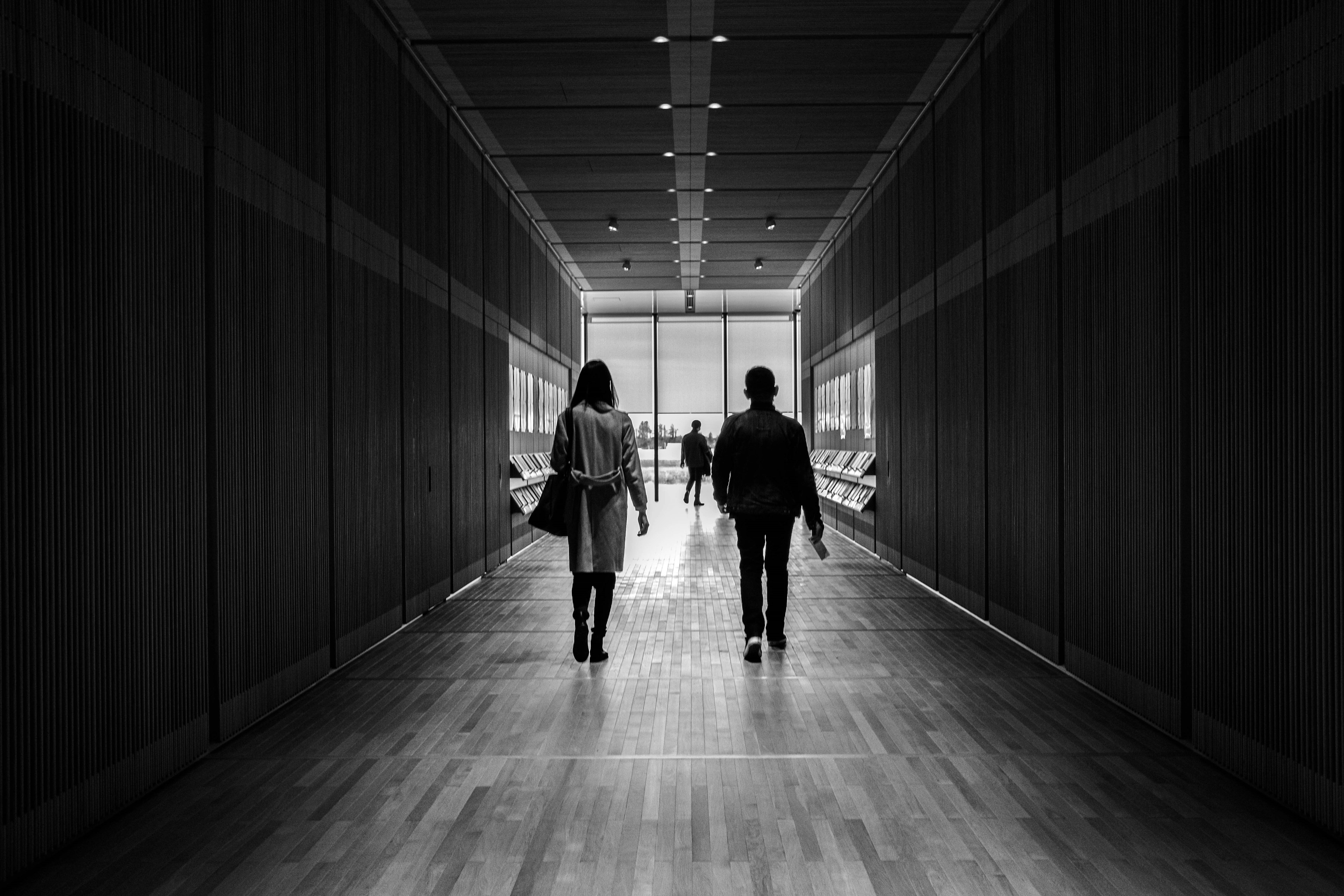 Two people walking in a black and white tunnel-like hallway