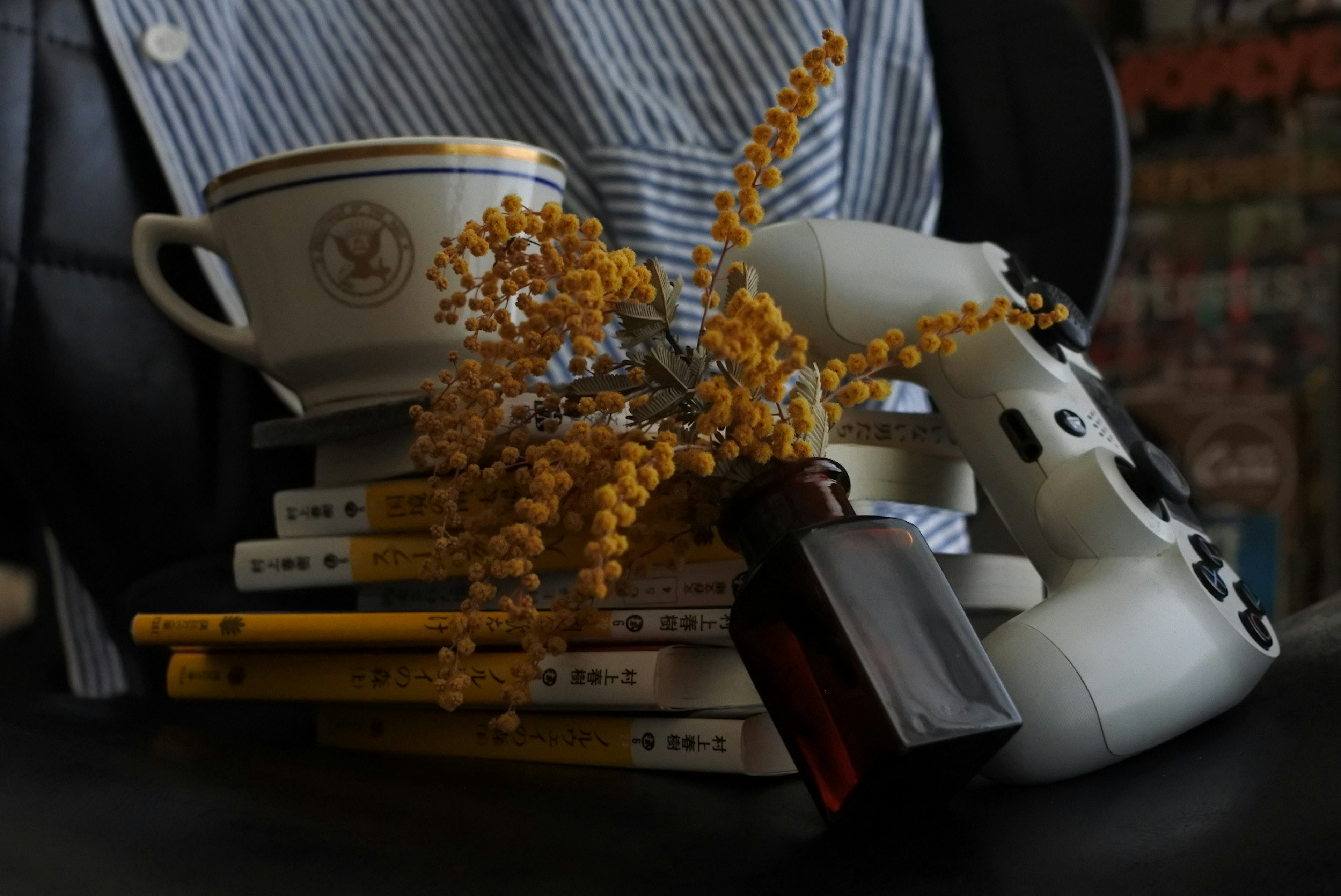 Un controller di gioco e un bouquet giallo sopra una pila di libri e una tazza