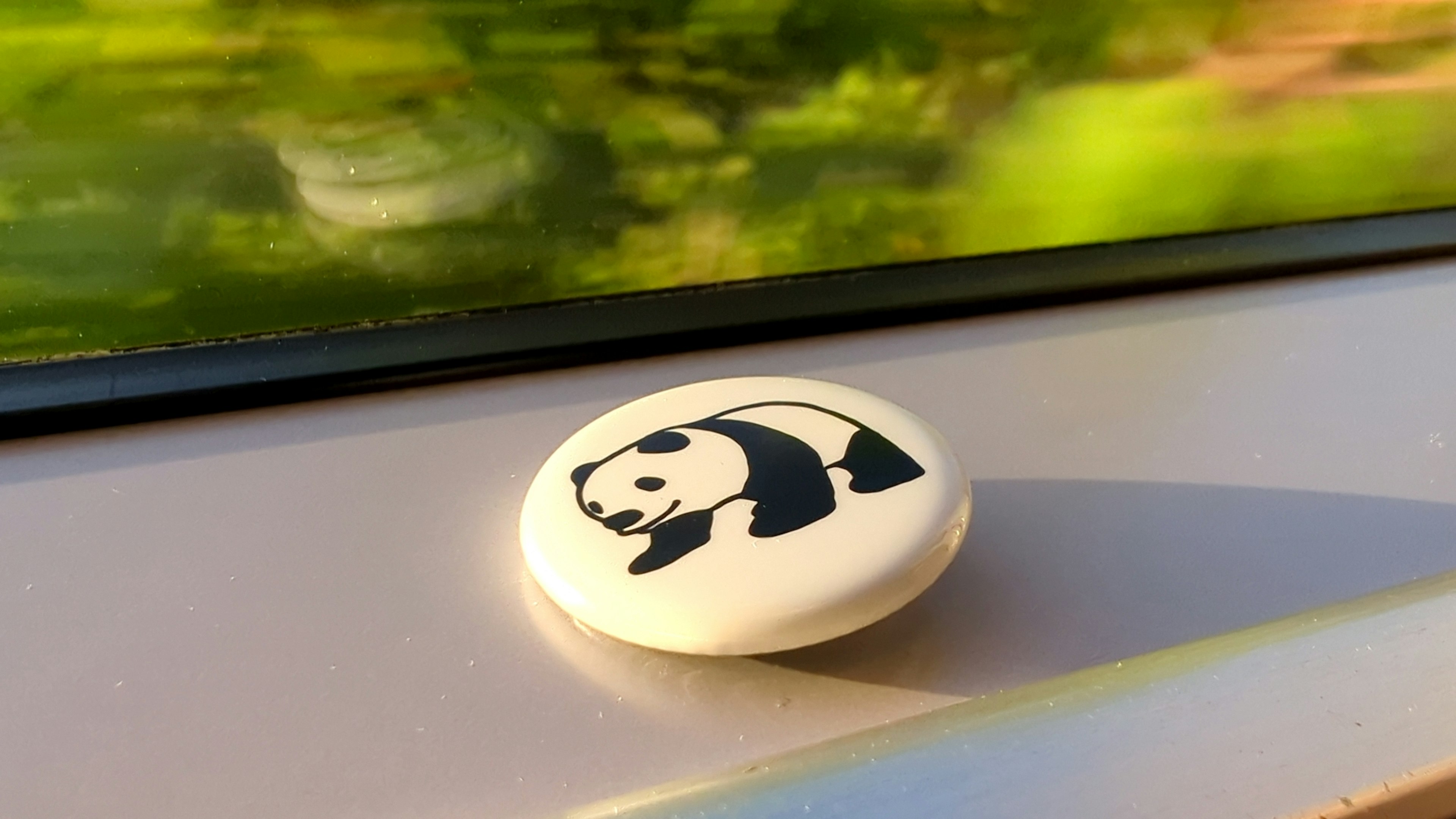 Ein weißer Knopf mit einer Panda-Illustration vor grünem Hintergrund