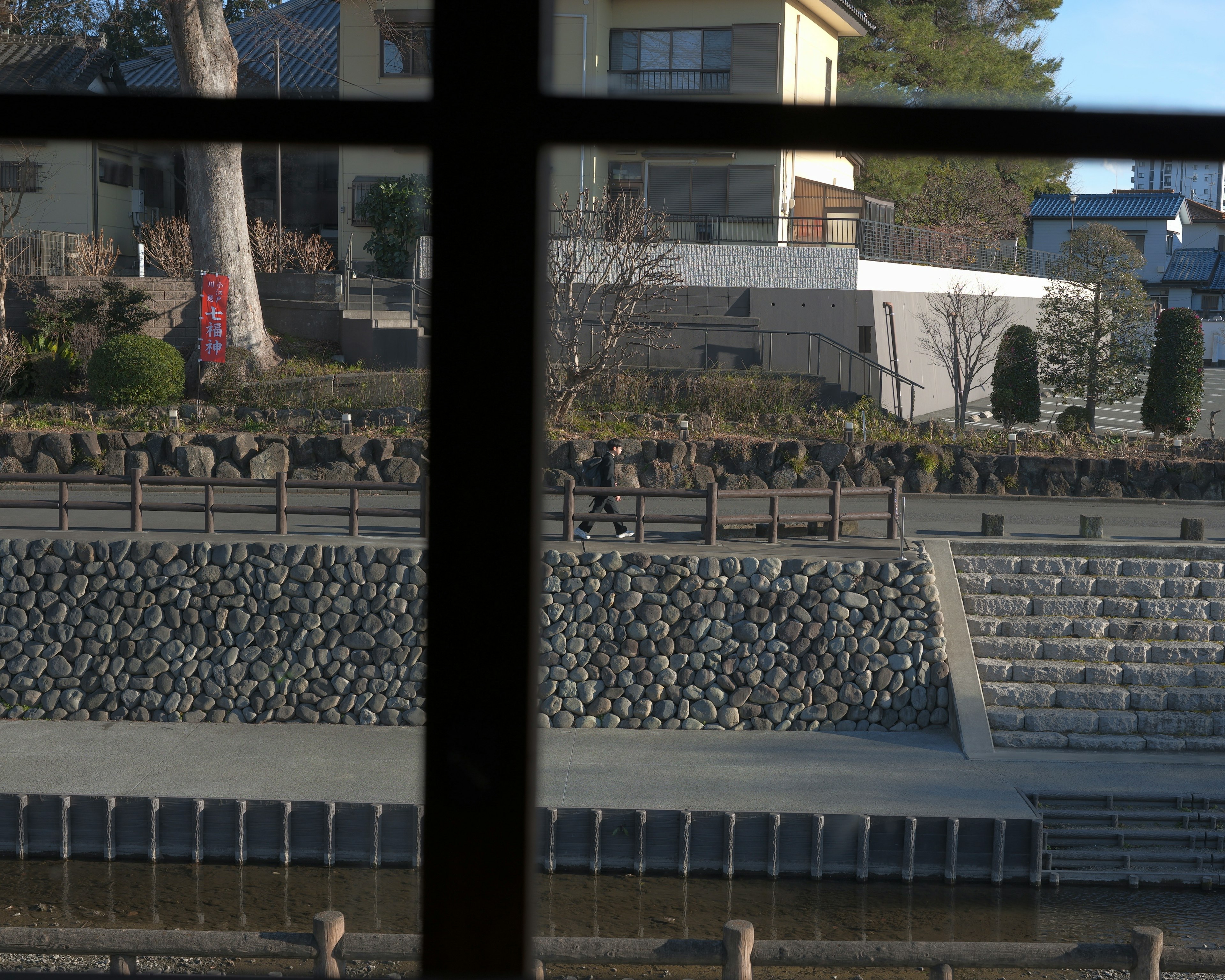 Vista a través de una ventana que muestra un jardín paisajístico con escaleras de piedra y vegetación circundante