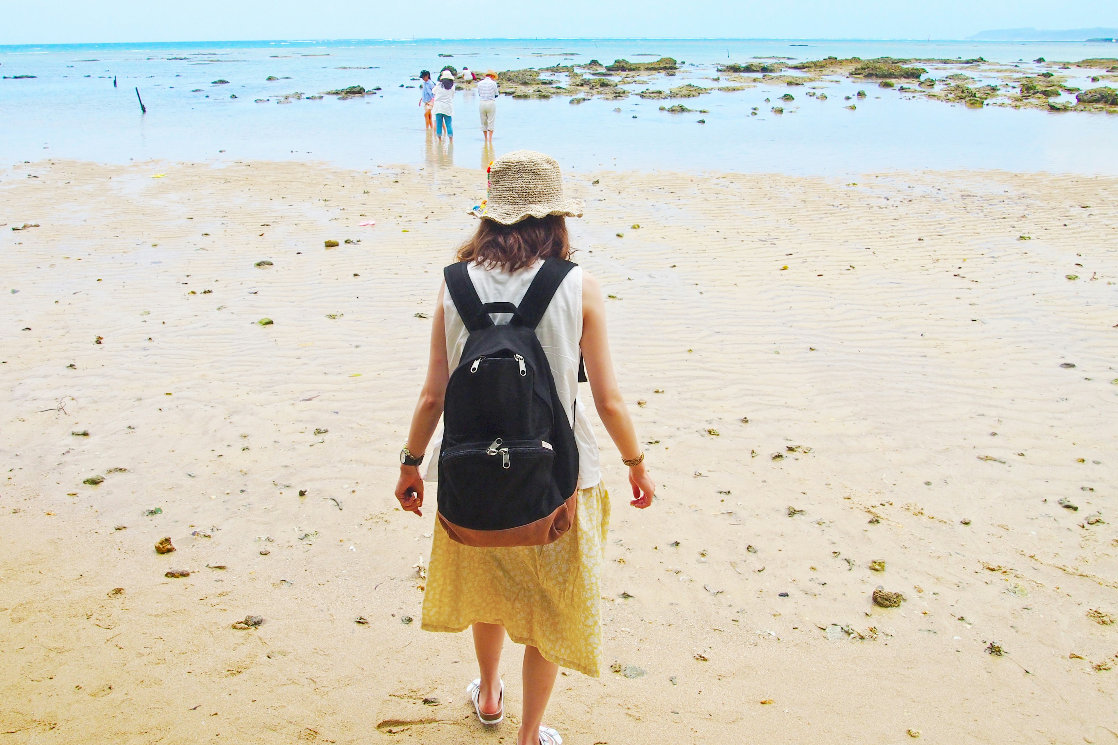 A woman walking on the beach wearing a backpack and a sun hat