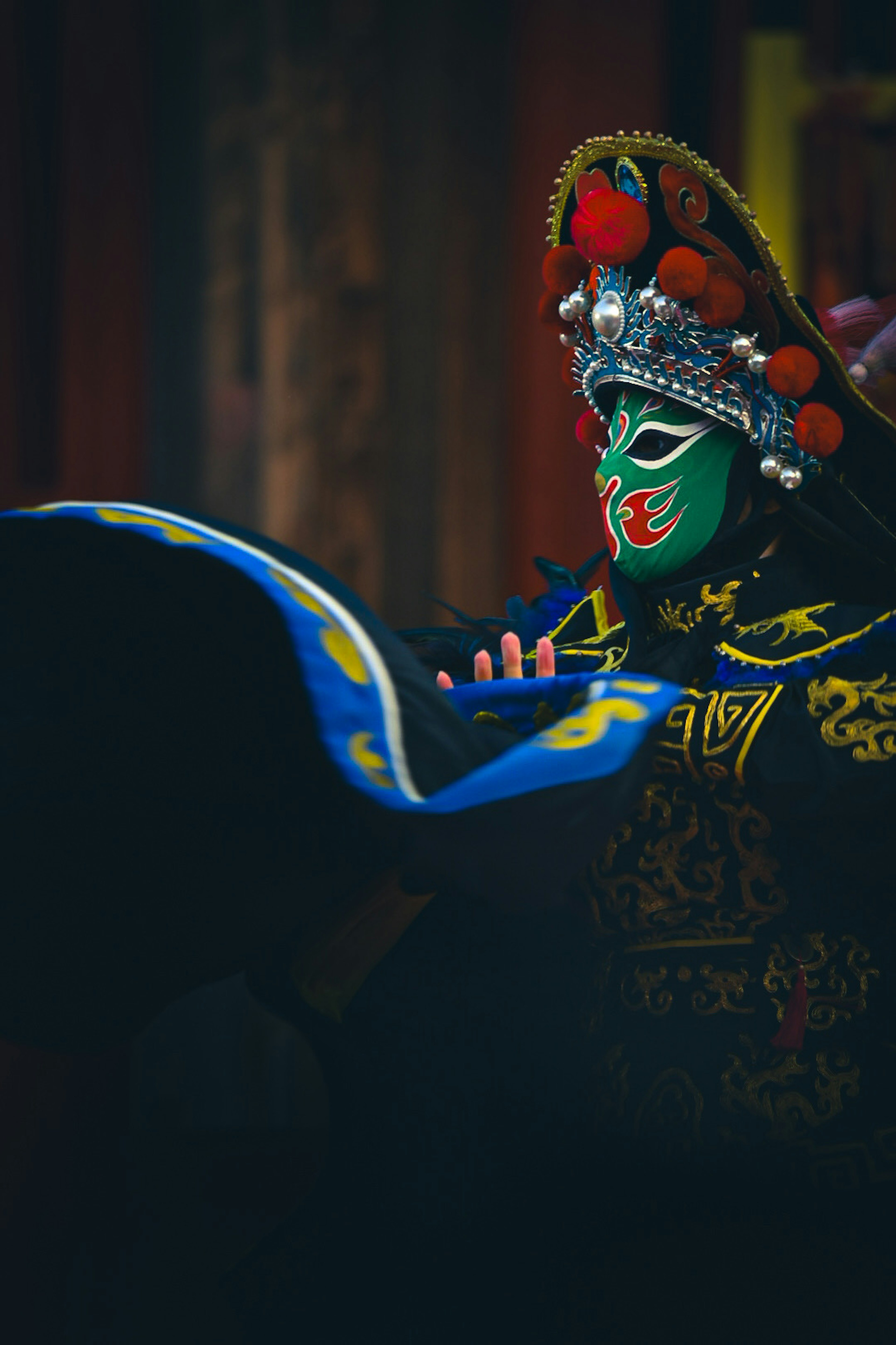 Une personne portant un habit traditionnel chinois tient un éventail bleu et a un masque vert