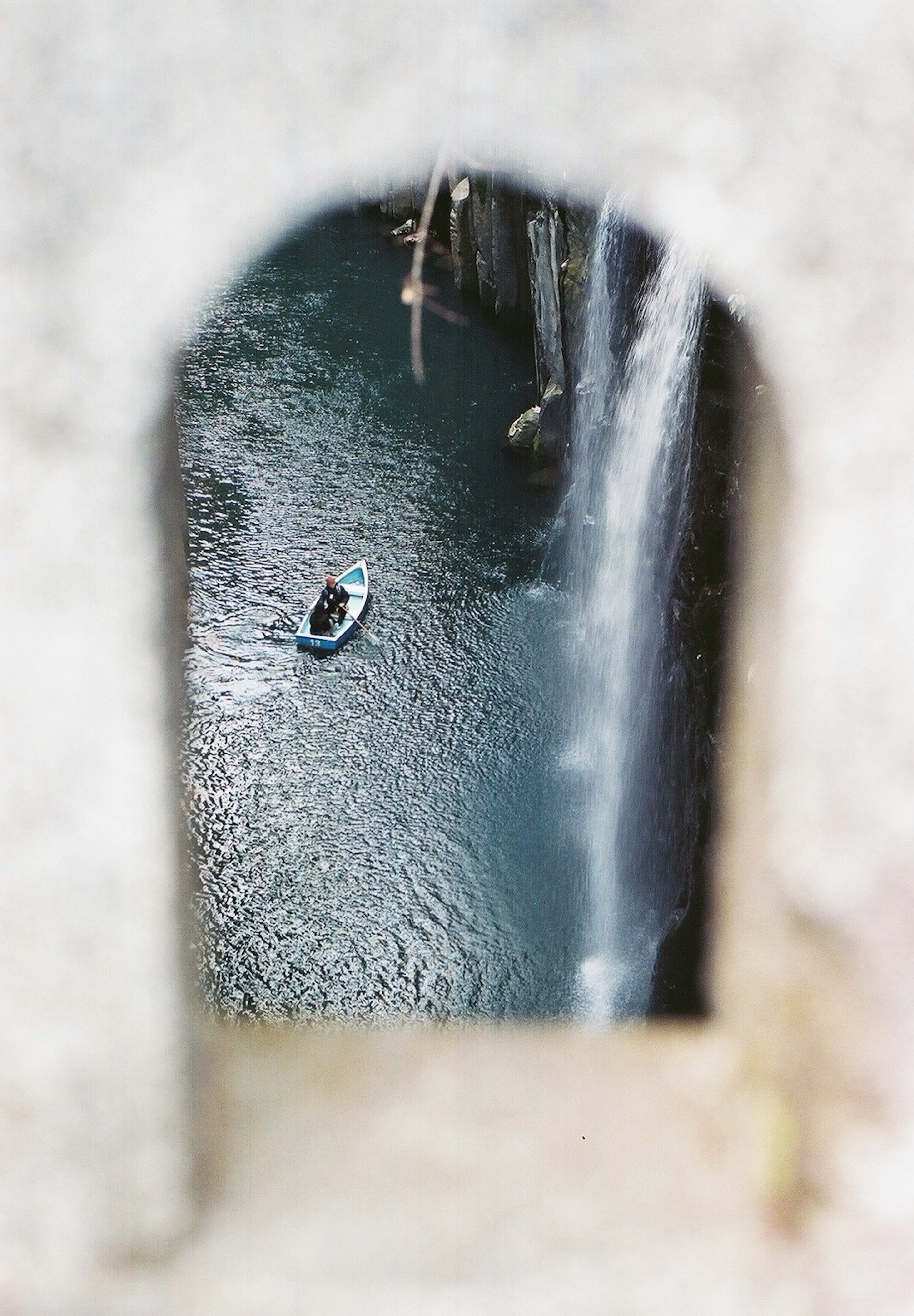 A person in a small boat on a river behind a waterfall