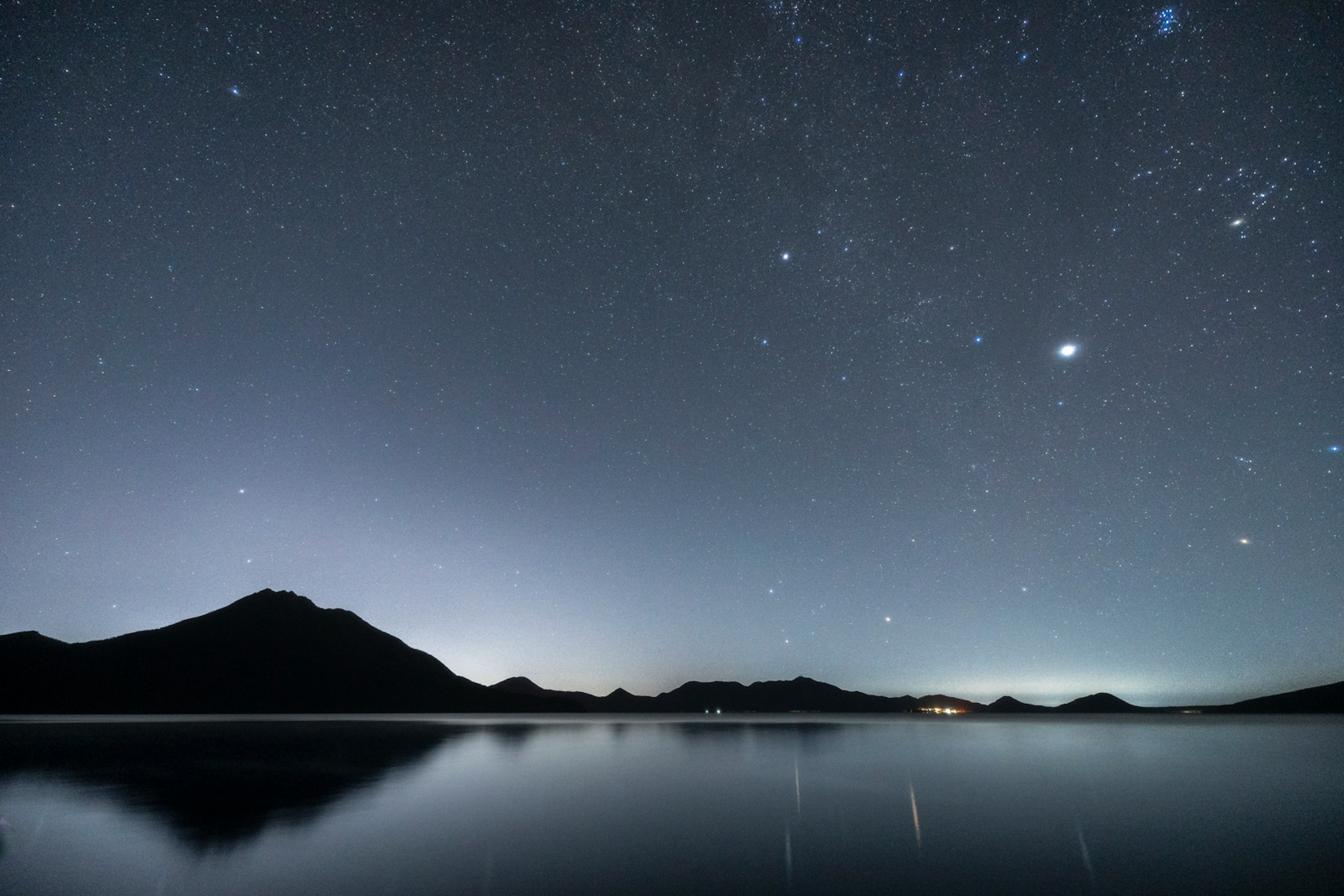 Langit berbintang di atas danau tenang dengan siluet gunung