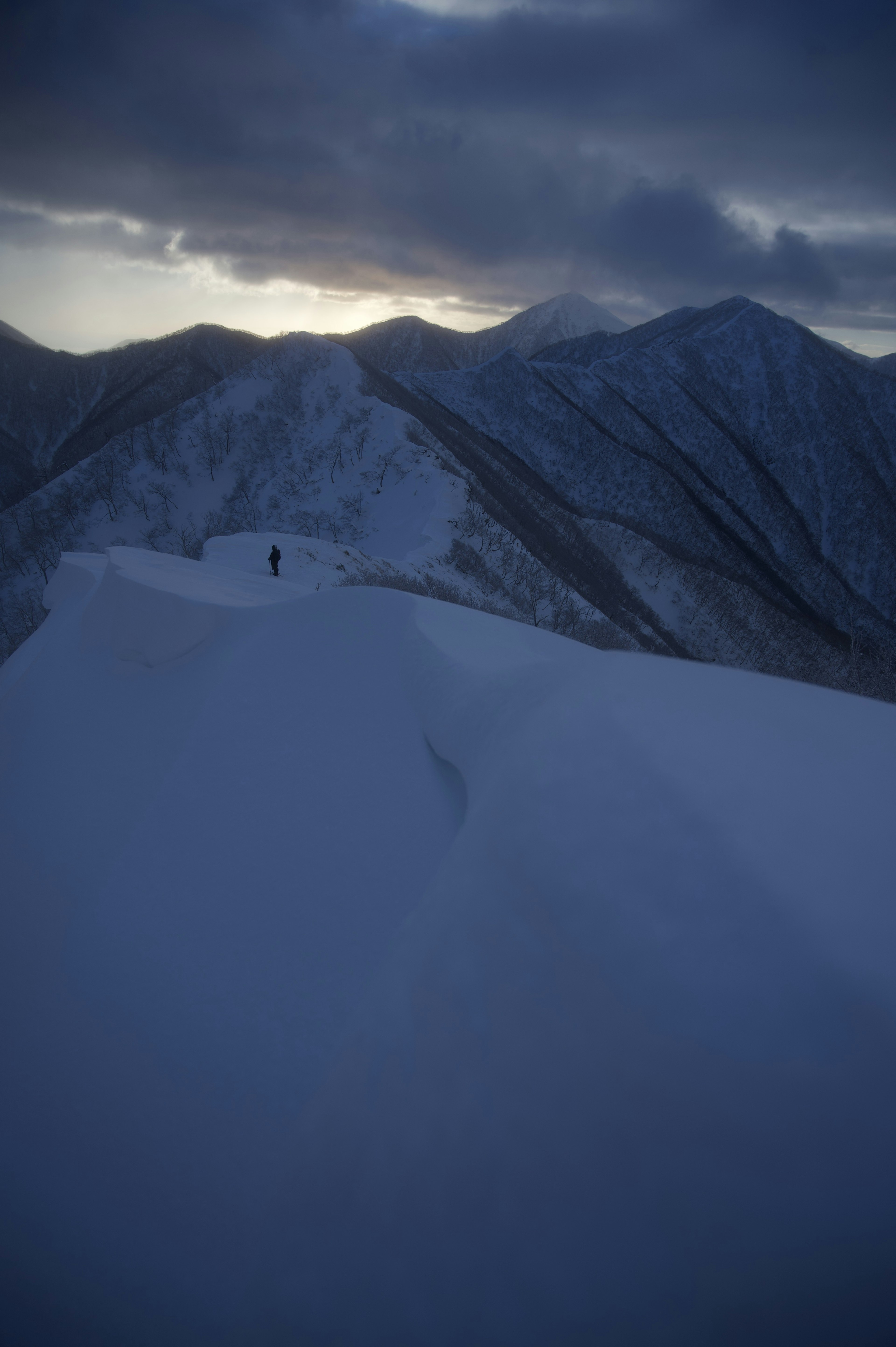 Silhouette di un alpinista in piedi su una cresta montuosa coperta di neve