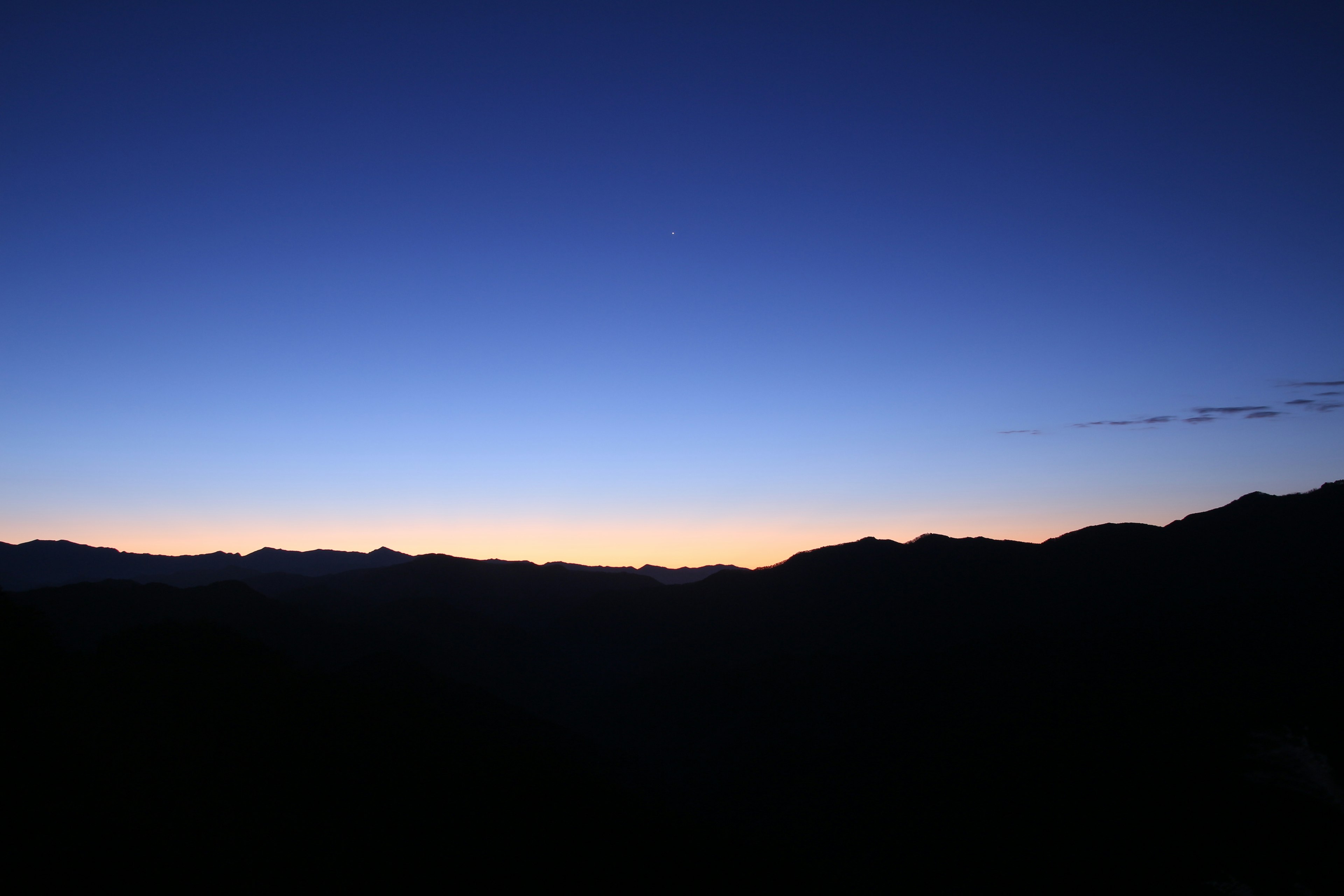 夜明けの静かな山のシルエットと青い空