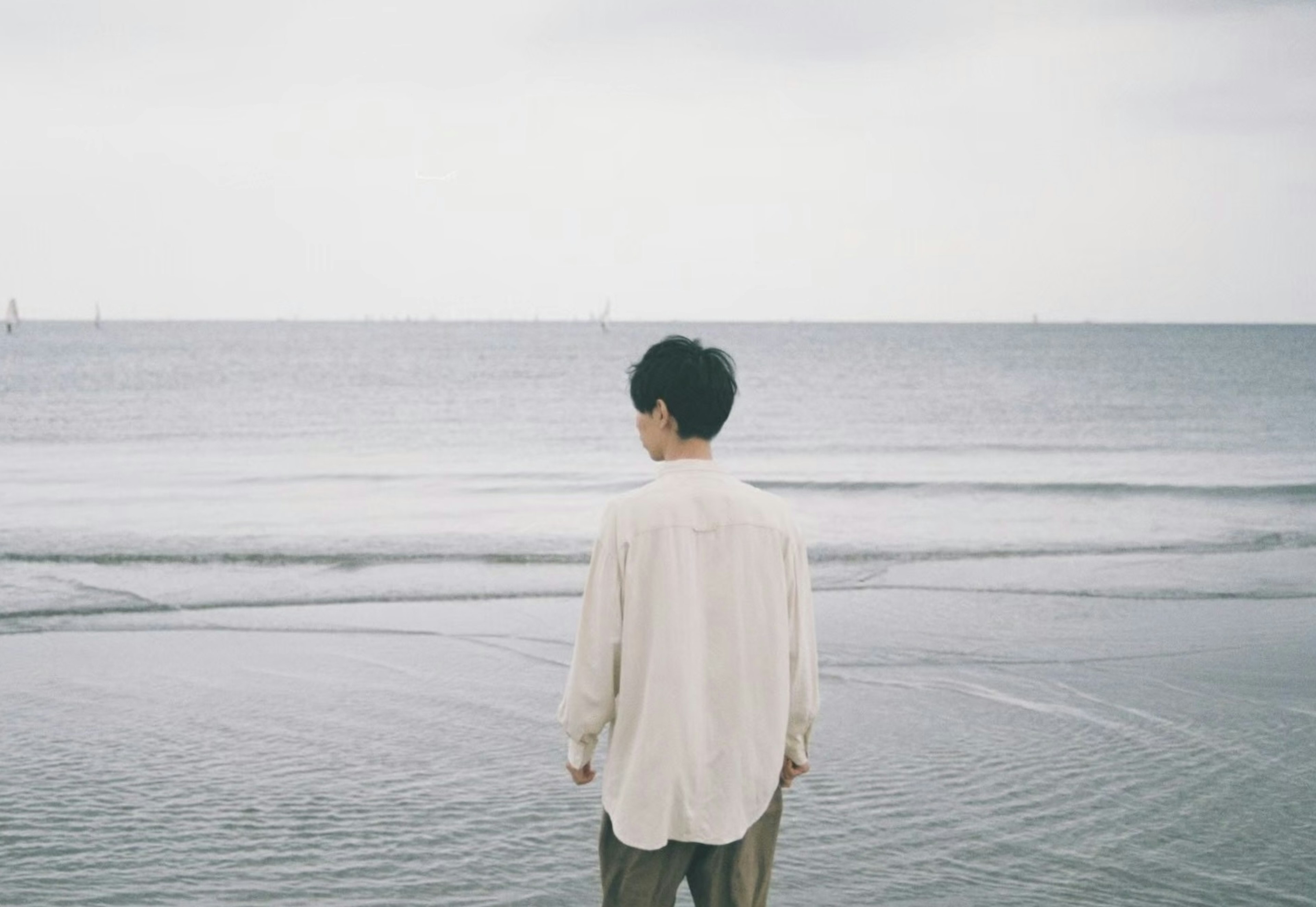 Homme se tenant au bord de la mer sous un ciel nuageux et des eaux calmes