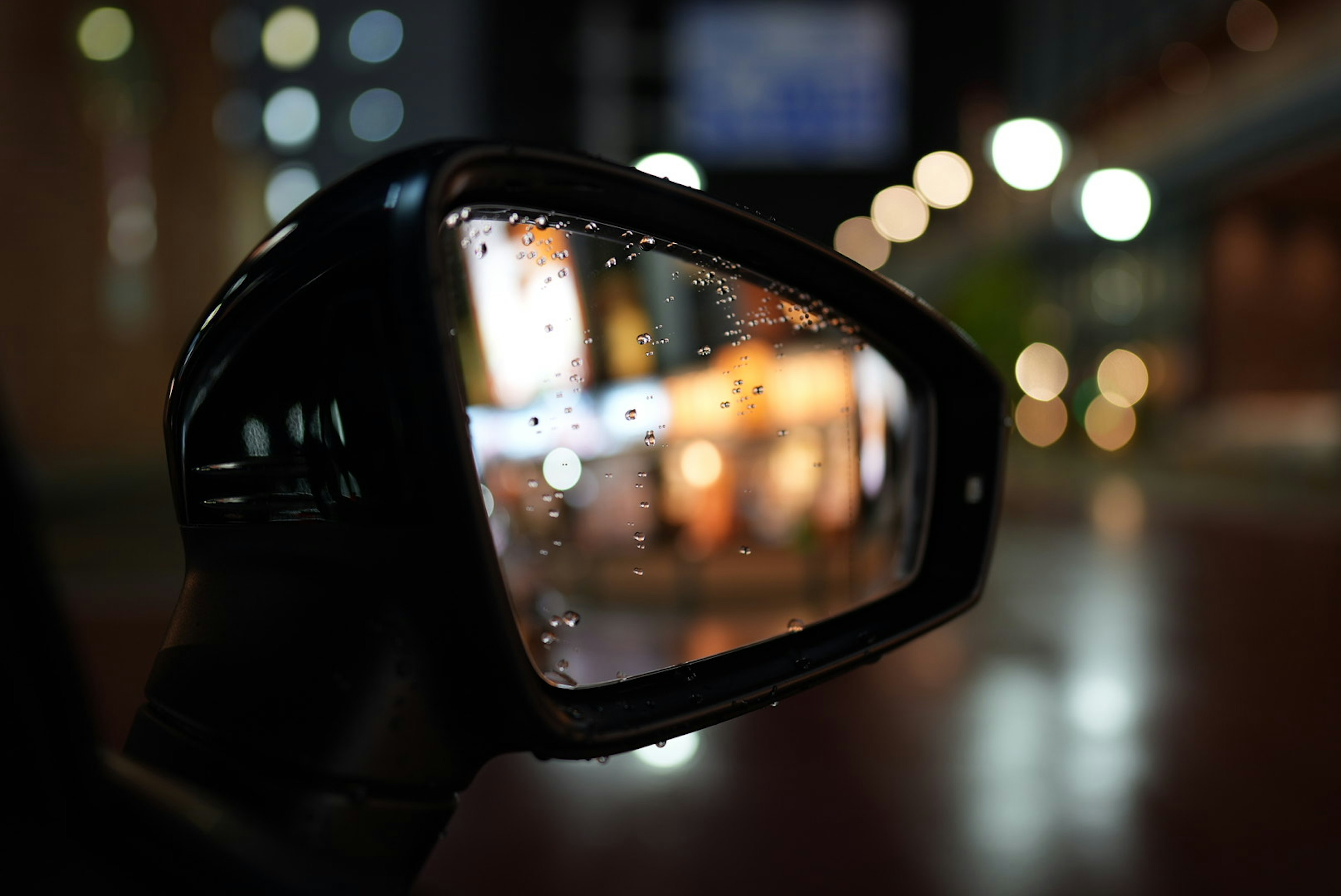 雨滴がついた車のサイドミラー 夜の街並みのぼやけた光が映る