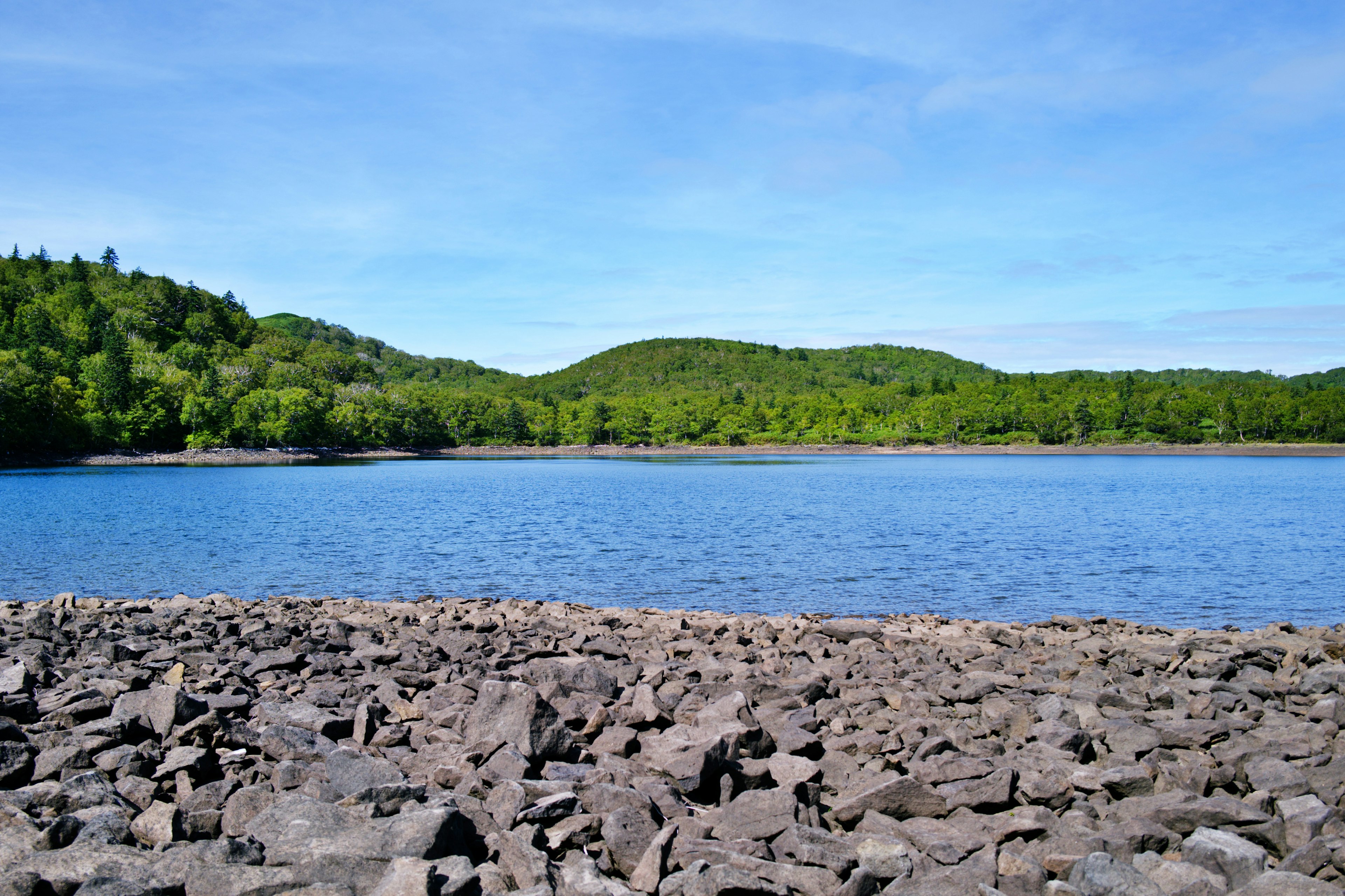 Vista escénica de un lago azul rodeado de colinas verdes orilla rocosa