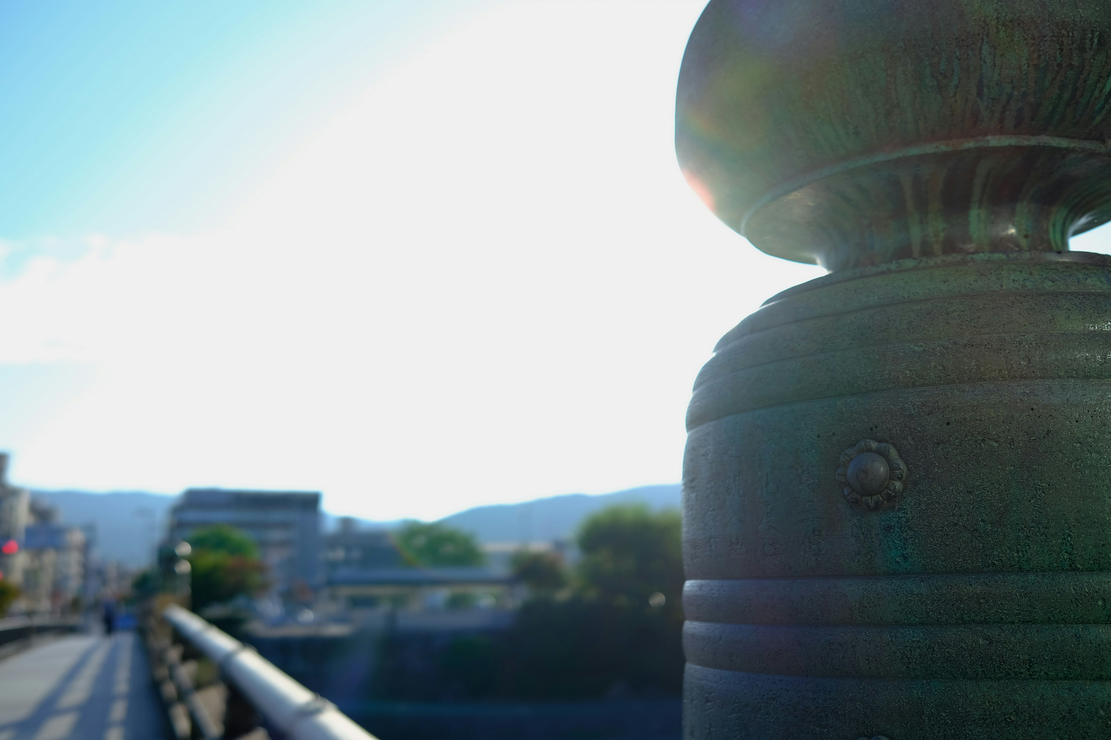 Brückenhandlauf mit Sonnenlicht und Gebäuden im Hintergrund