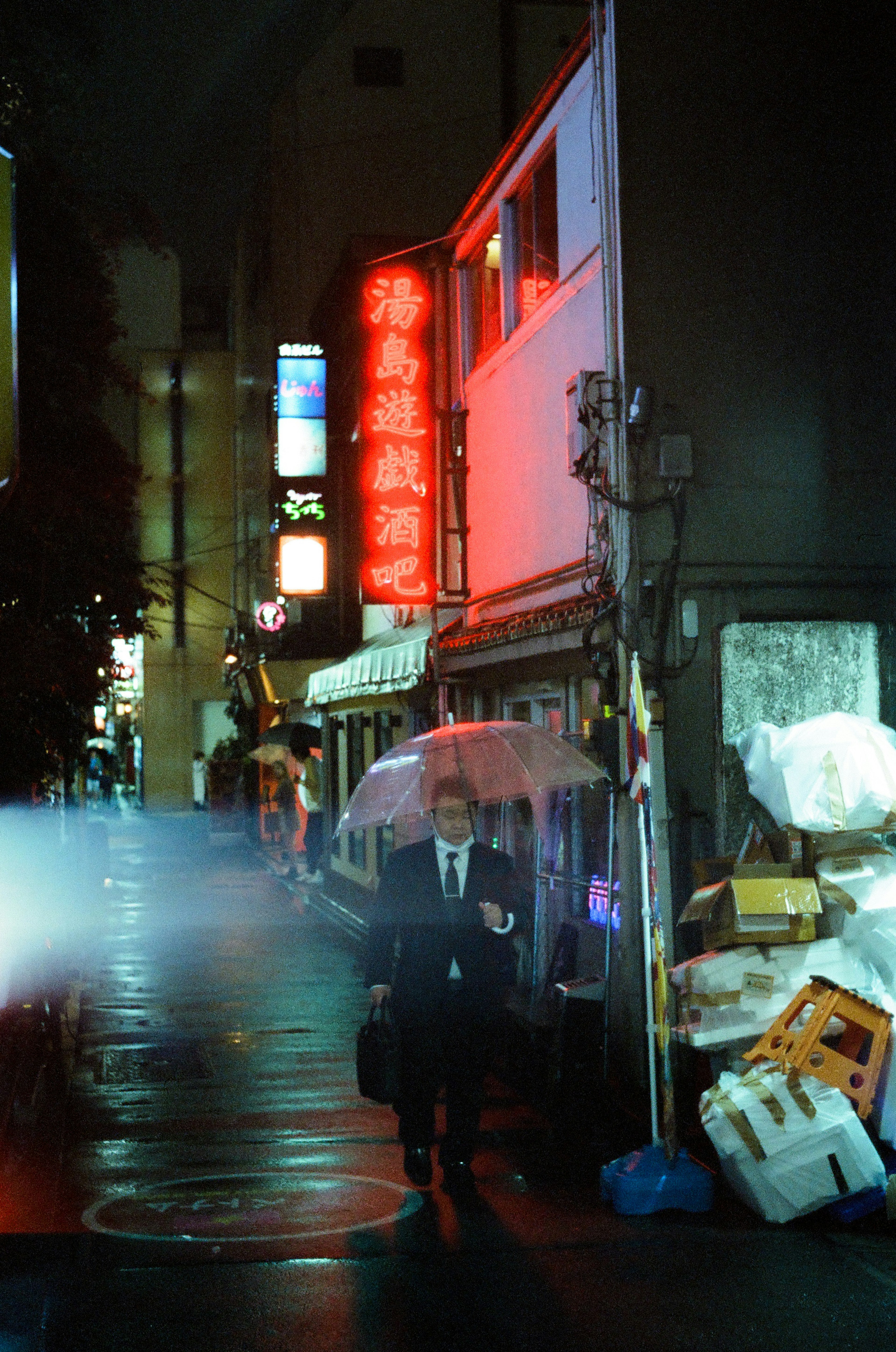 Un homme en costume marchant sous la pluie avec des enseignes lumineuses dans une ville nocturne