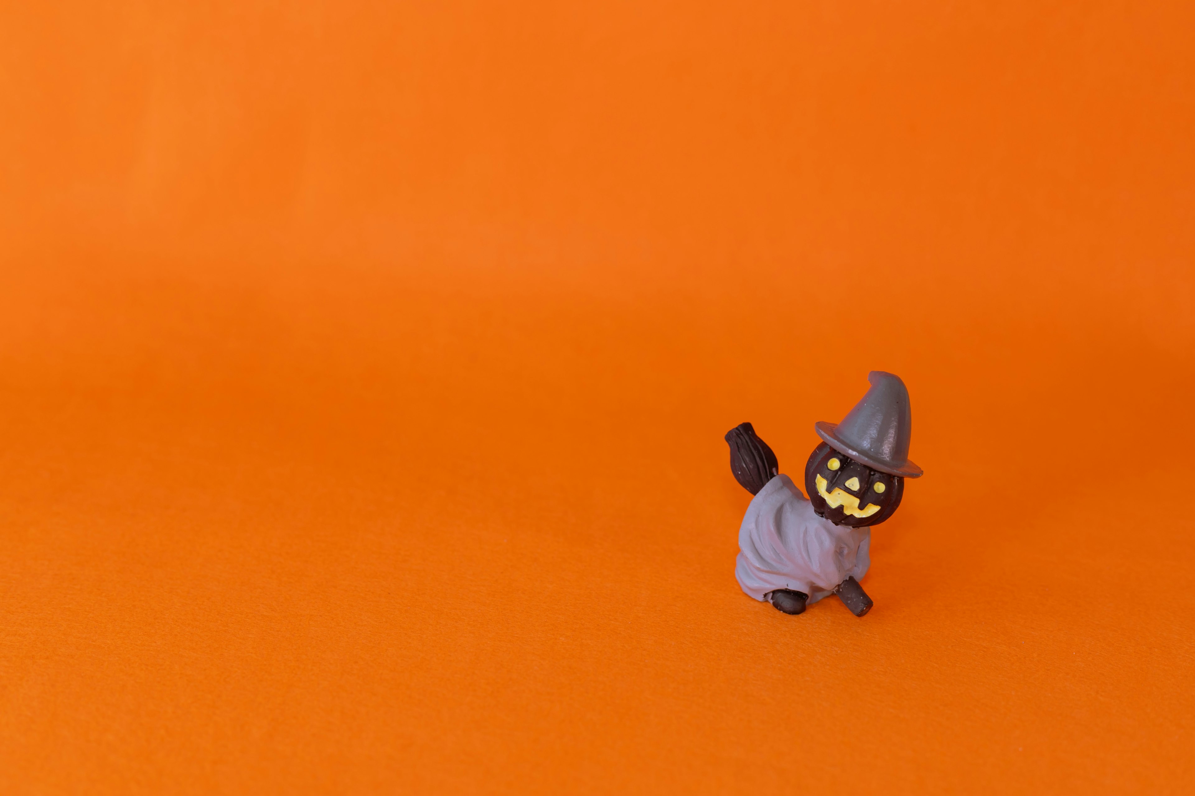 Small black witch figurine standing against an orange background