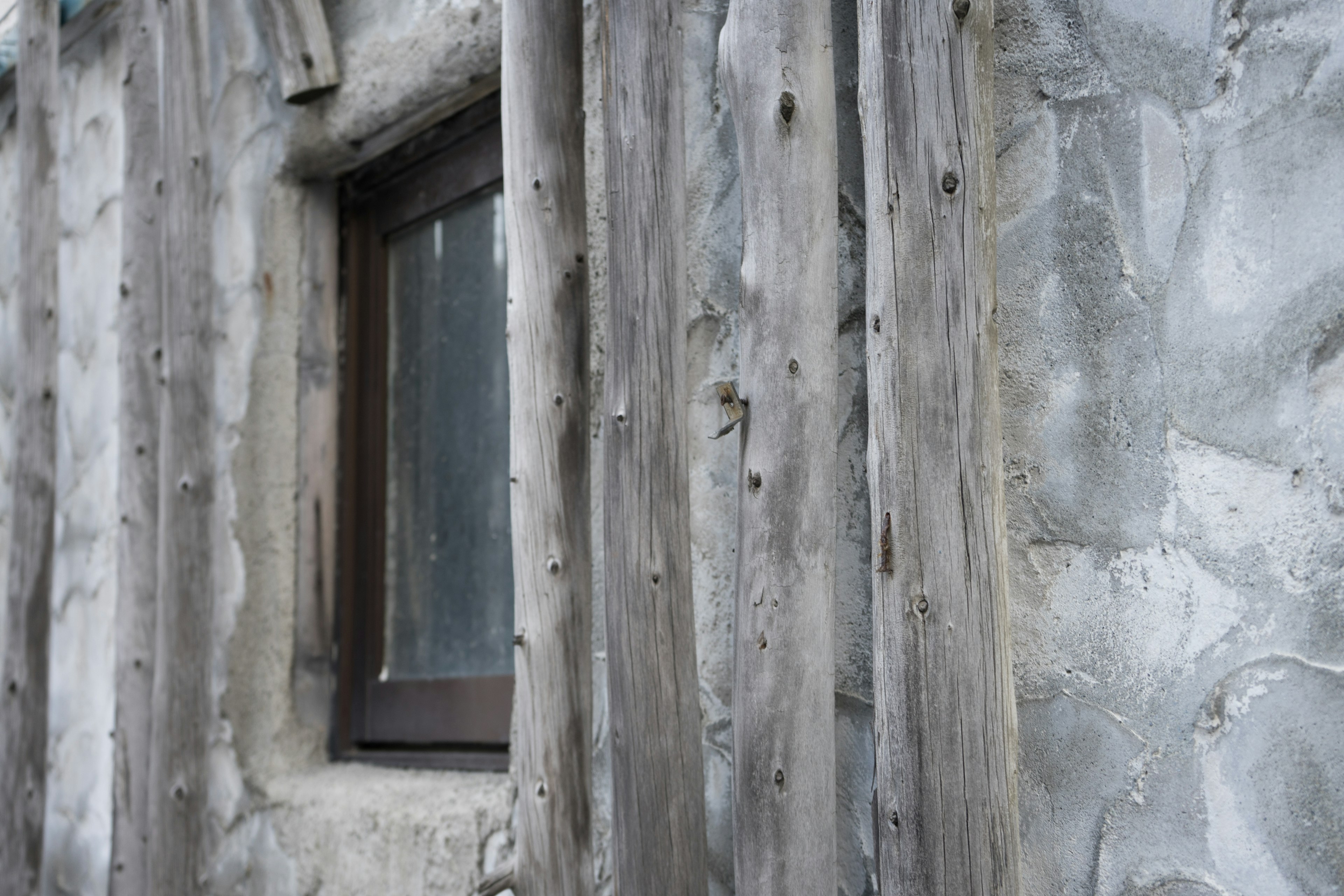 Close-up of a window framed by weathered wood against a textured wall