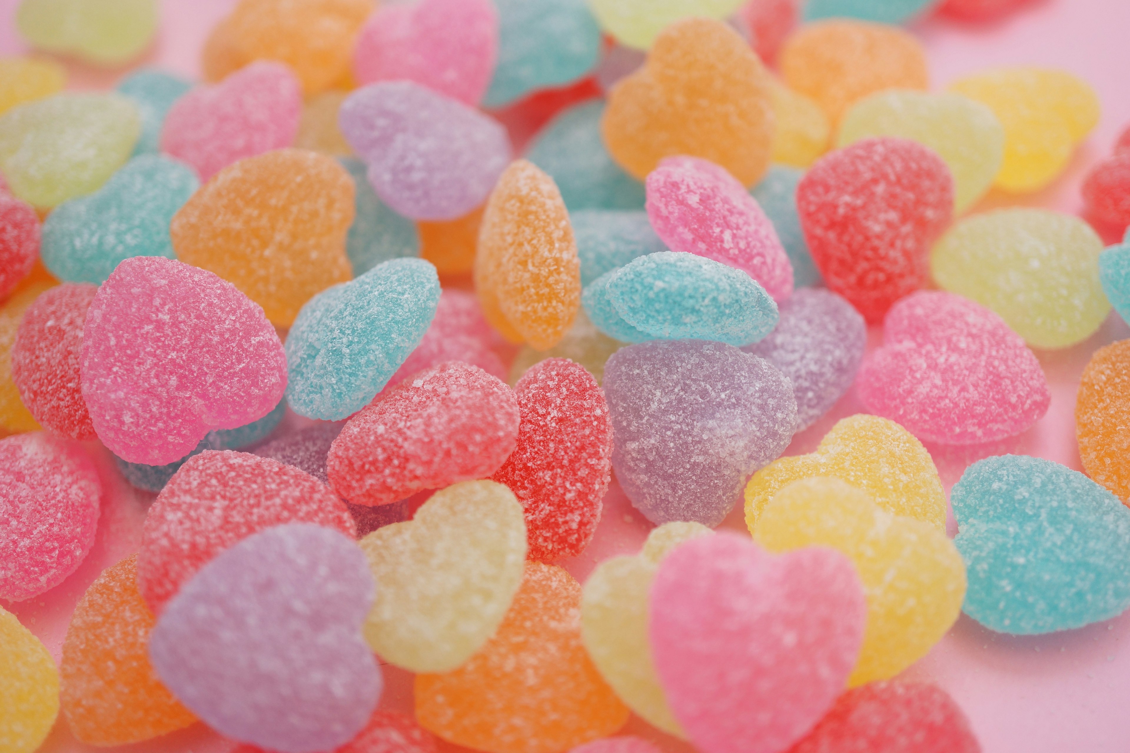 Colorful heart-shaped gummy candies scattered on a pink background