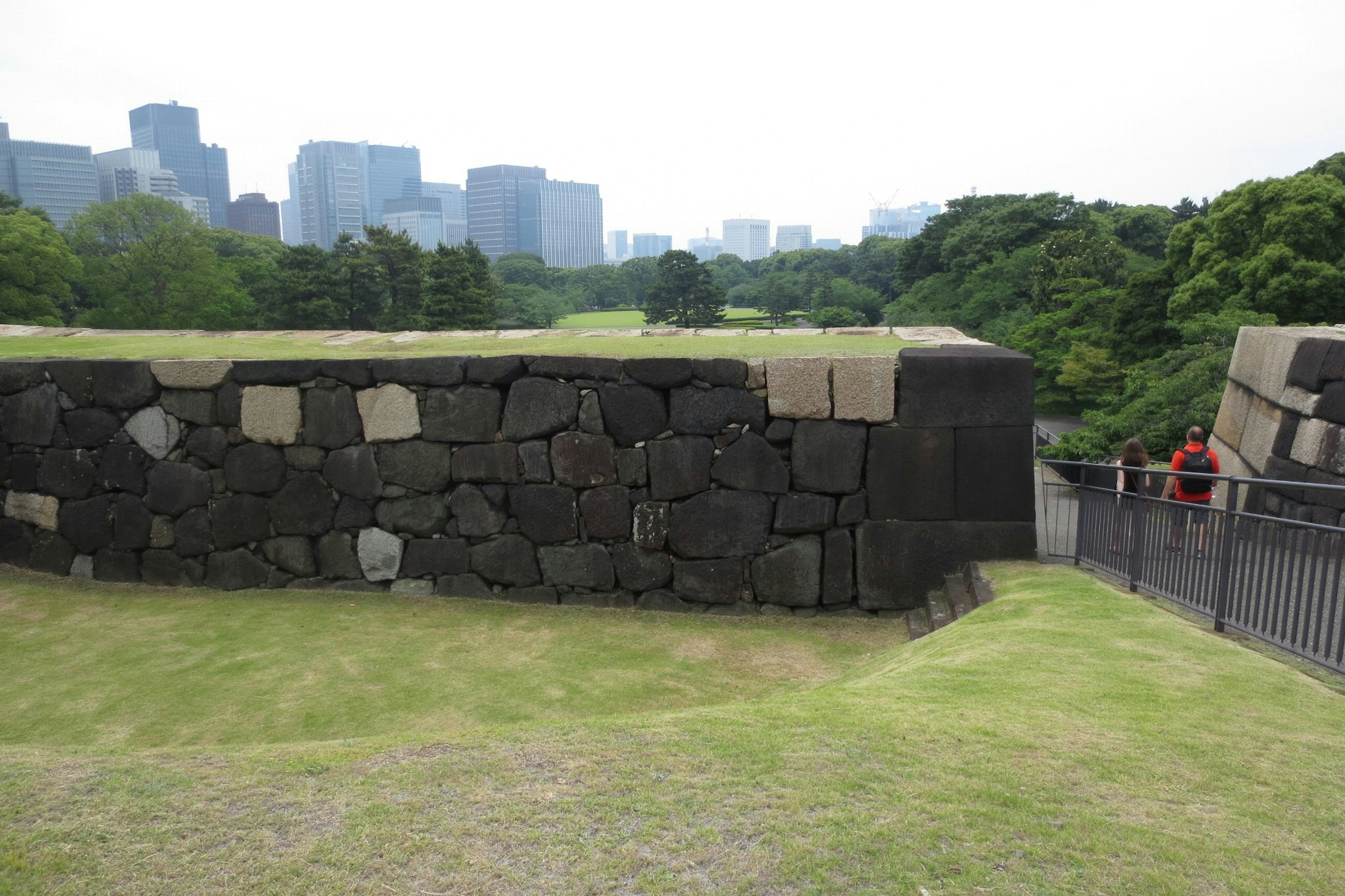 Muro di pietra con un parco lussureggiante e skyline moderna sullo sfondo