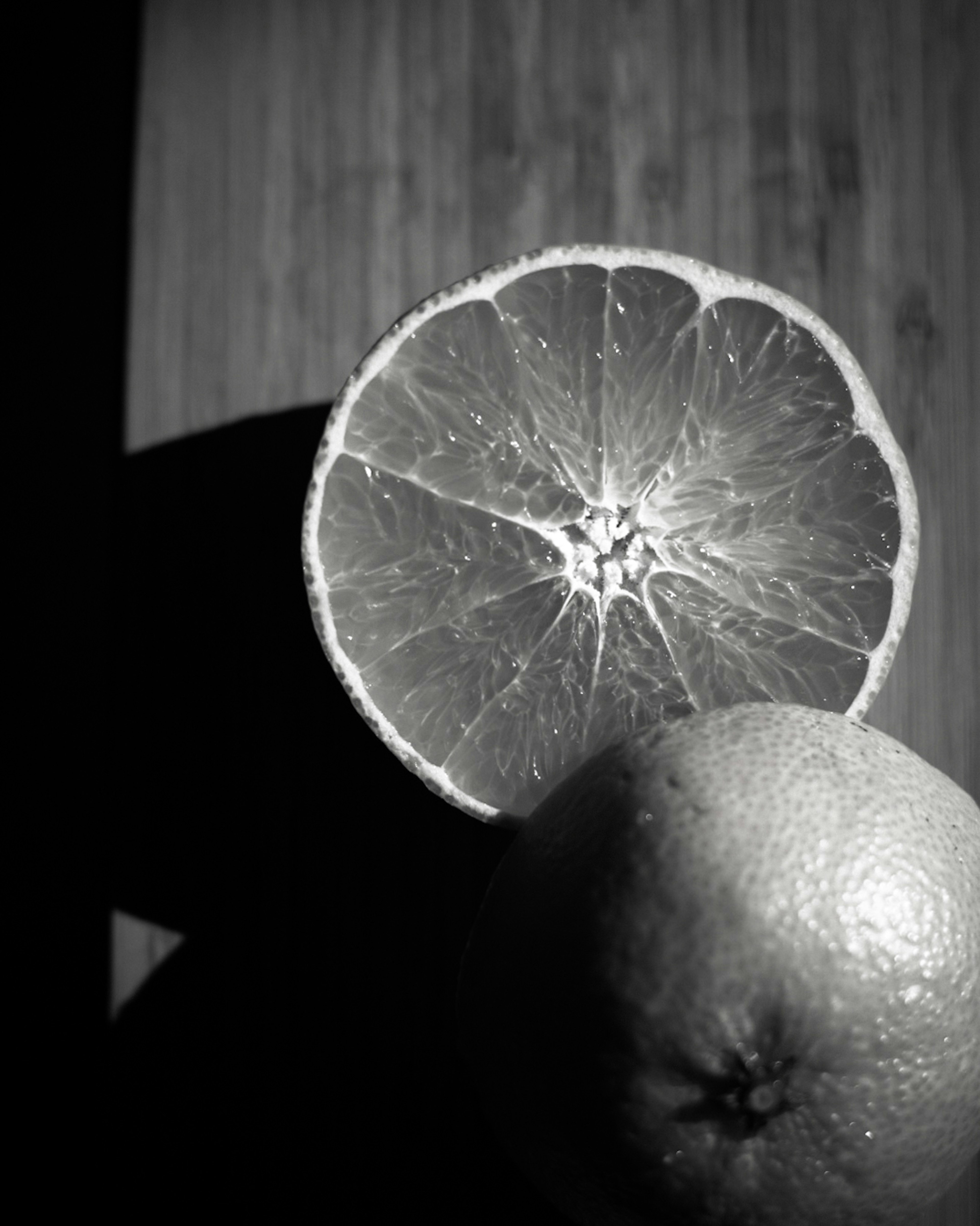 Black and white image of an orange and a halved orange on a wooden surface