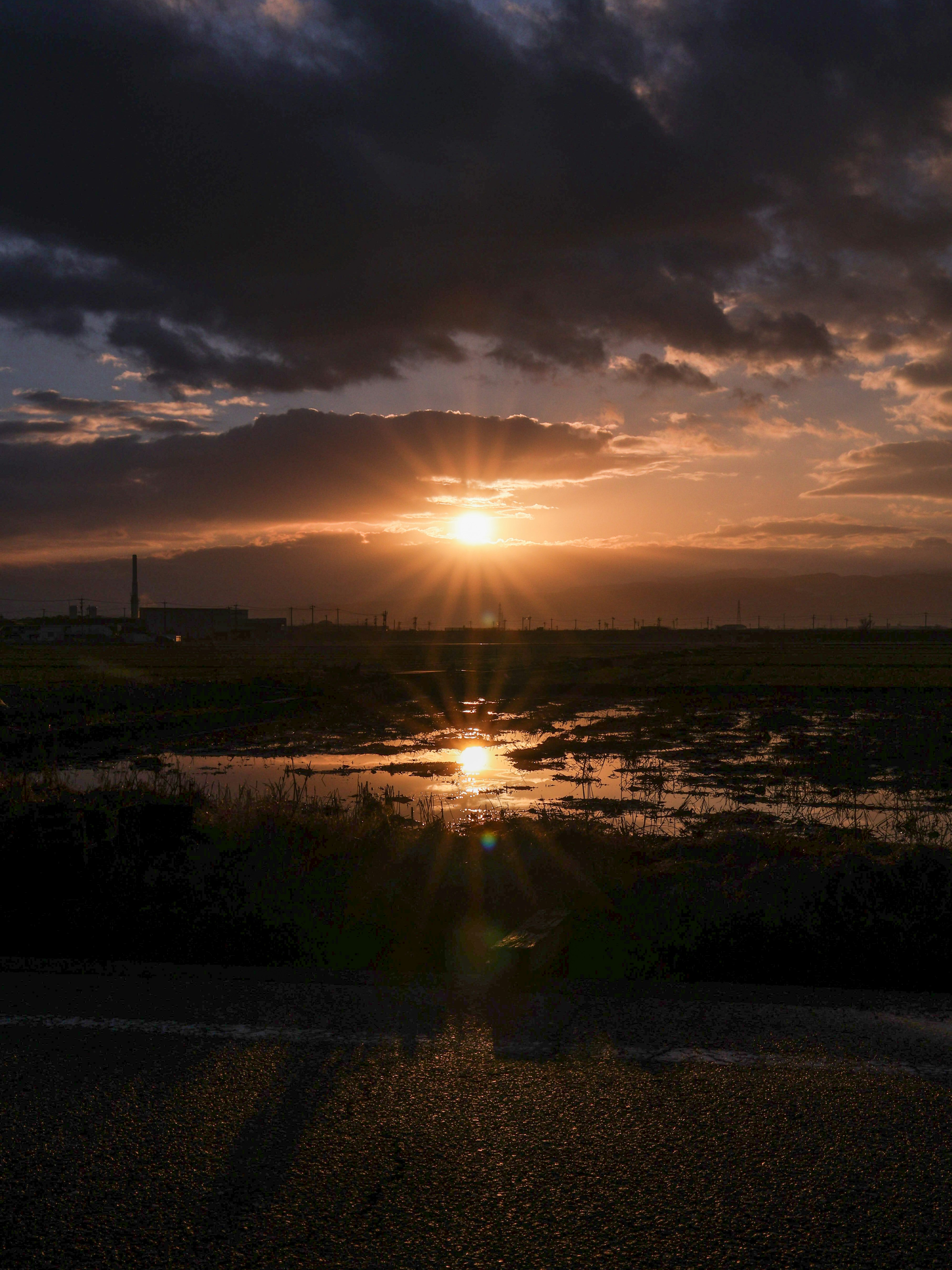 夕日が雲の隙間から輝く美しい風景 水面に反射する光と草原の景色