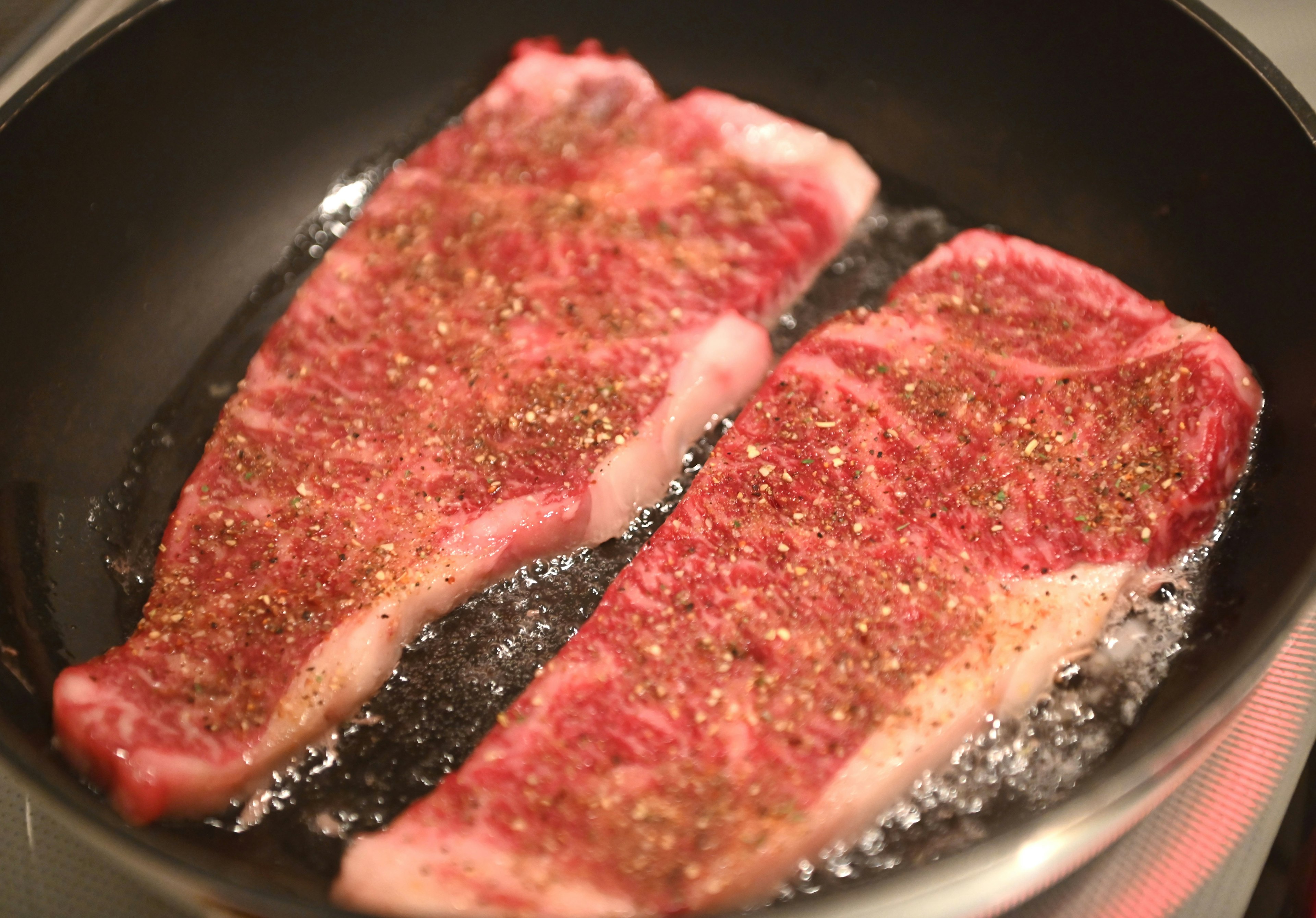 Two marbled beef steaks sizzling in a frying pan