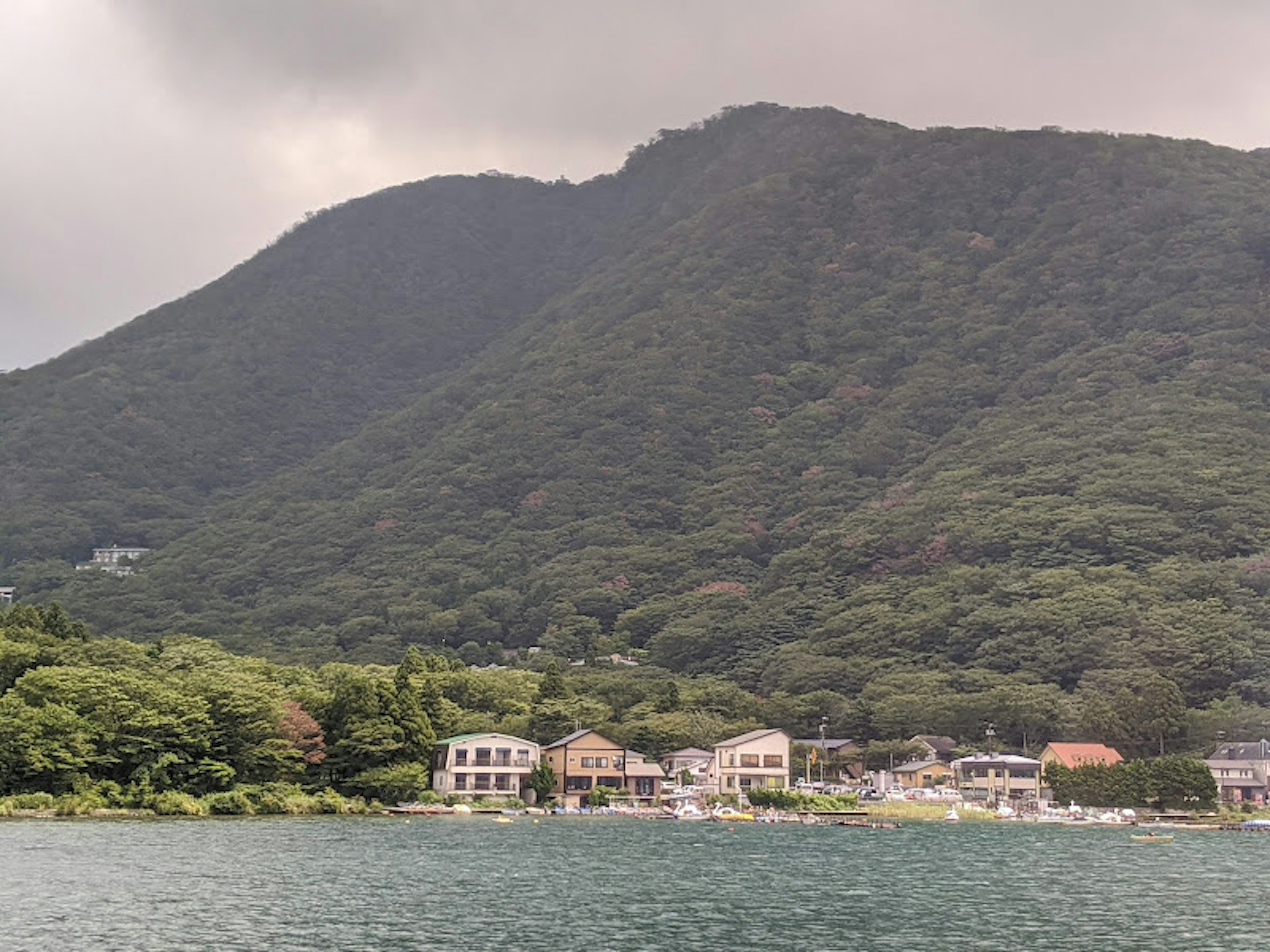 Danau tenang dengan rumah di latar depan dan latar belakang pegunungan