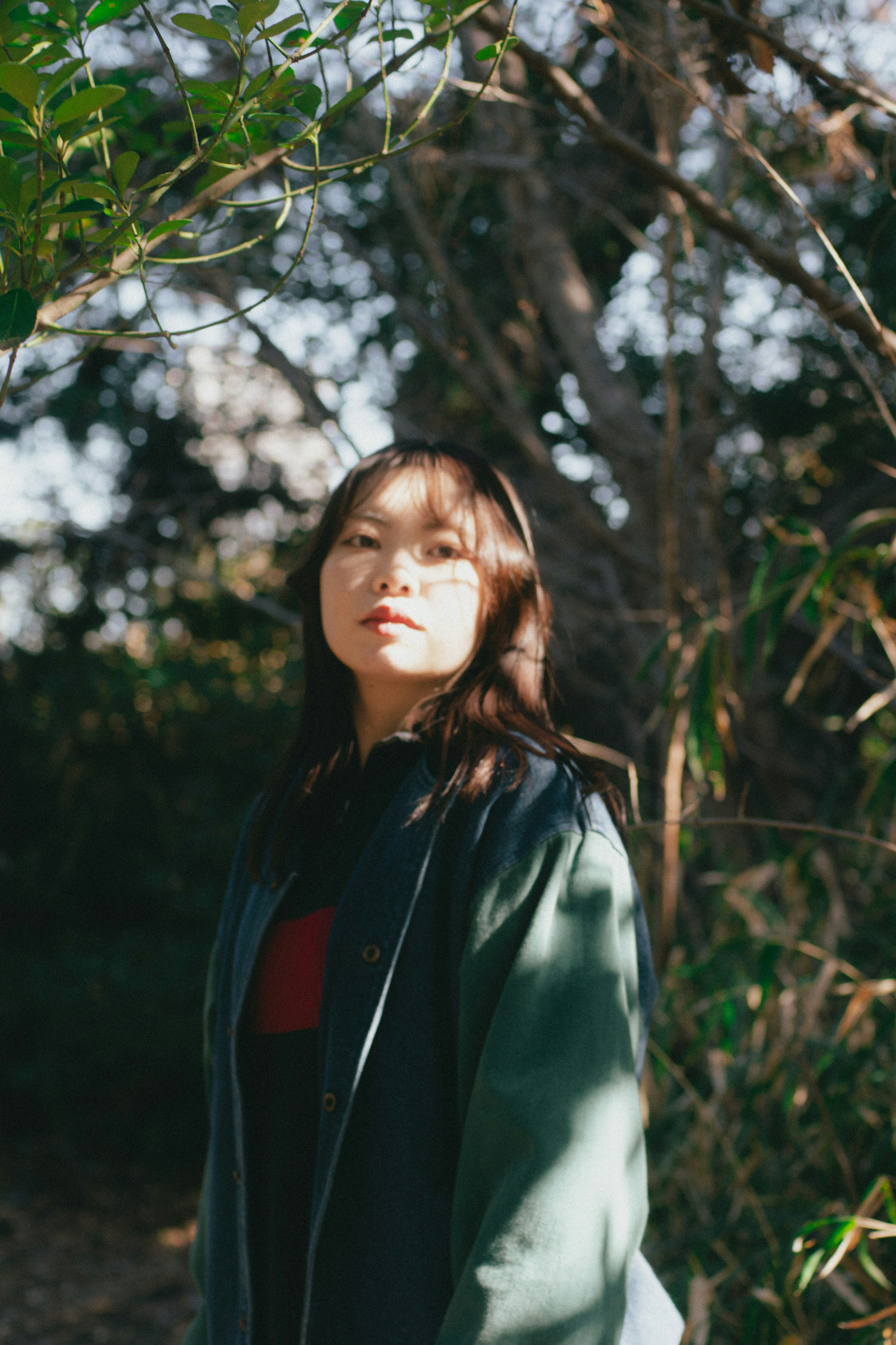 Femme en manteau vert se tenant au soleil entourée de verdure