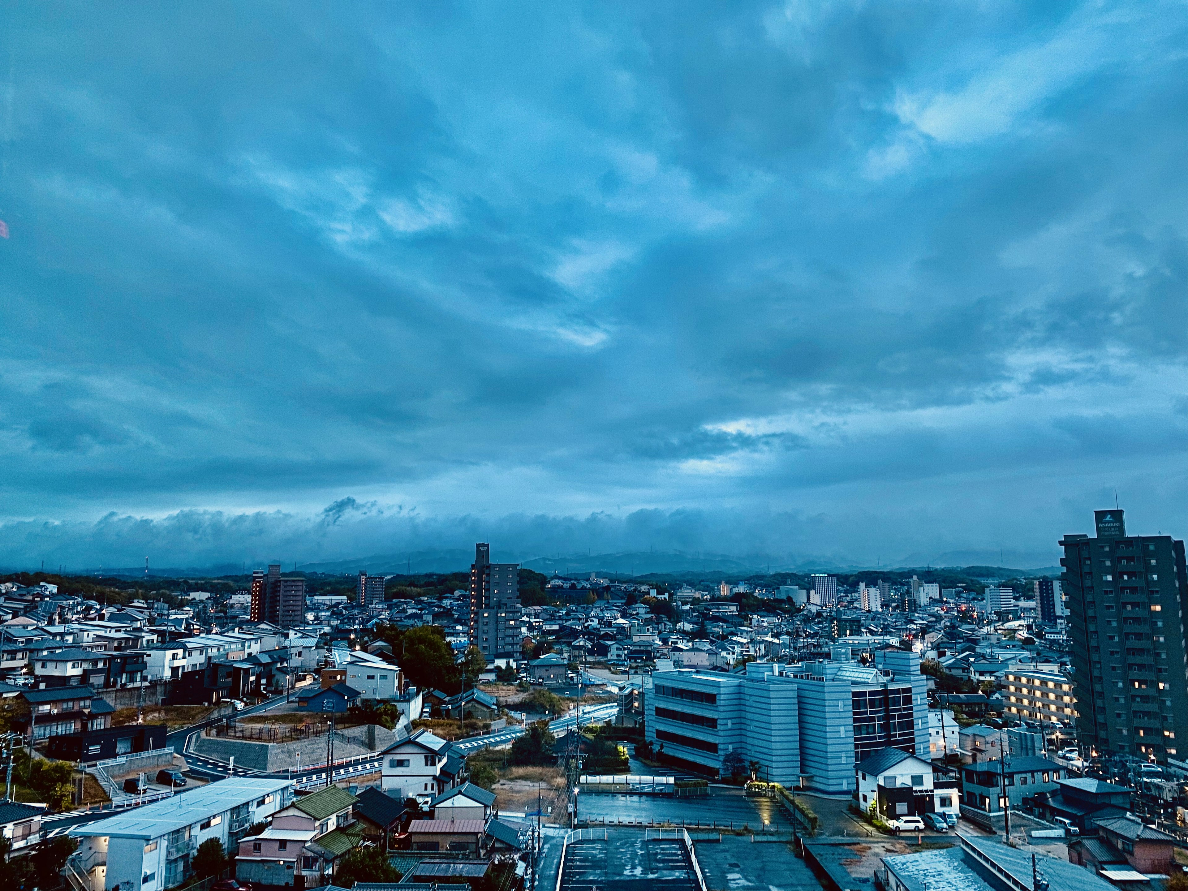 Pemandangan kota dengan langit biru dan awan menampilkan gedung tinggi dan rumah