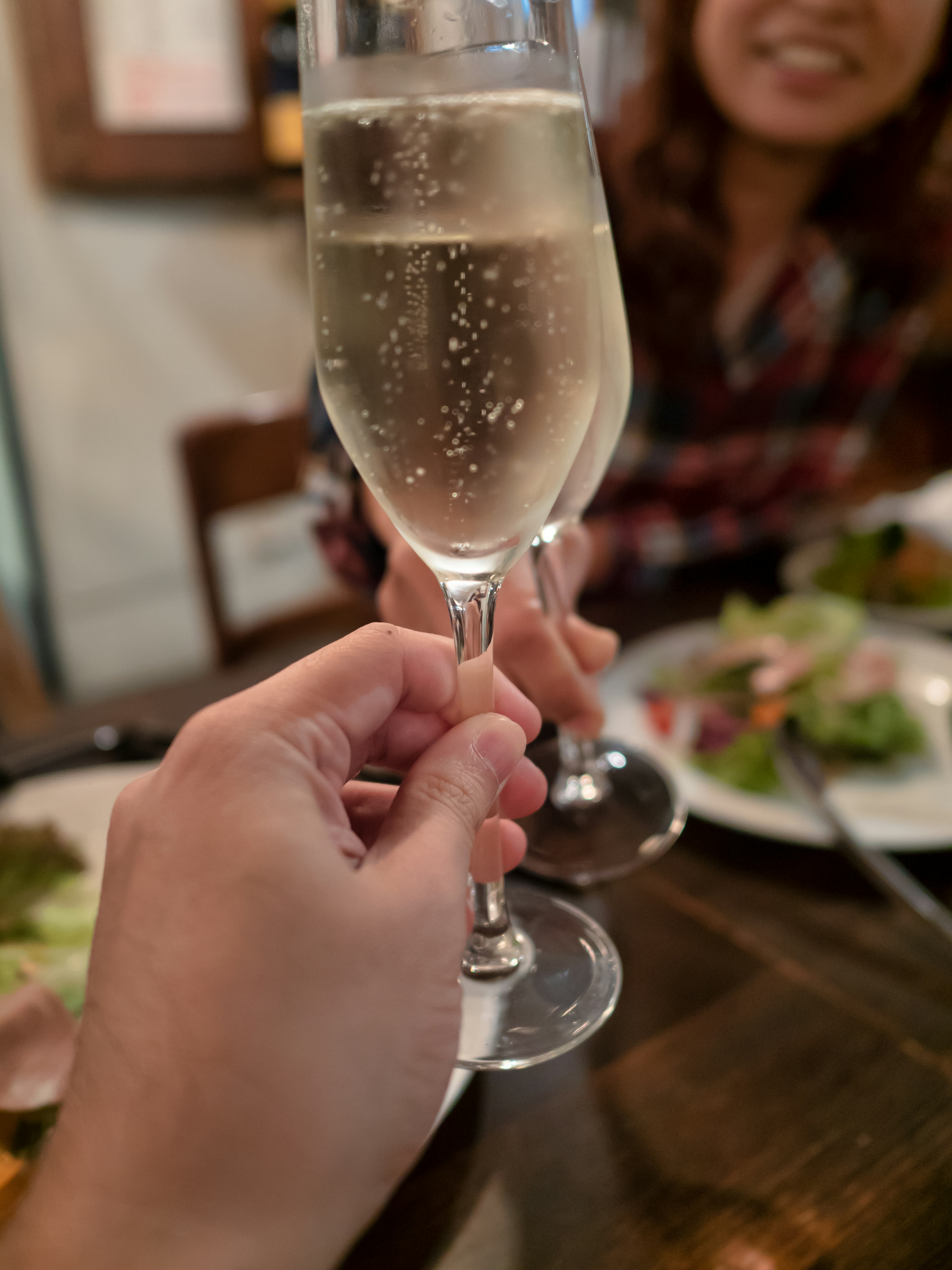 Hand holding a sparkling champagne glass with a smiling friend in the background