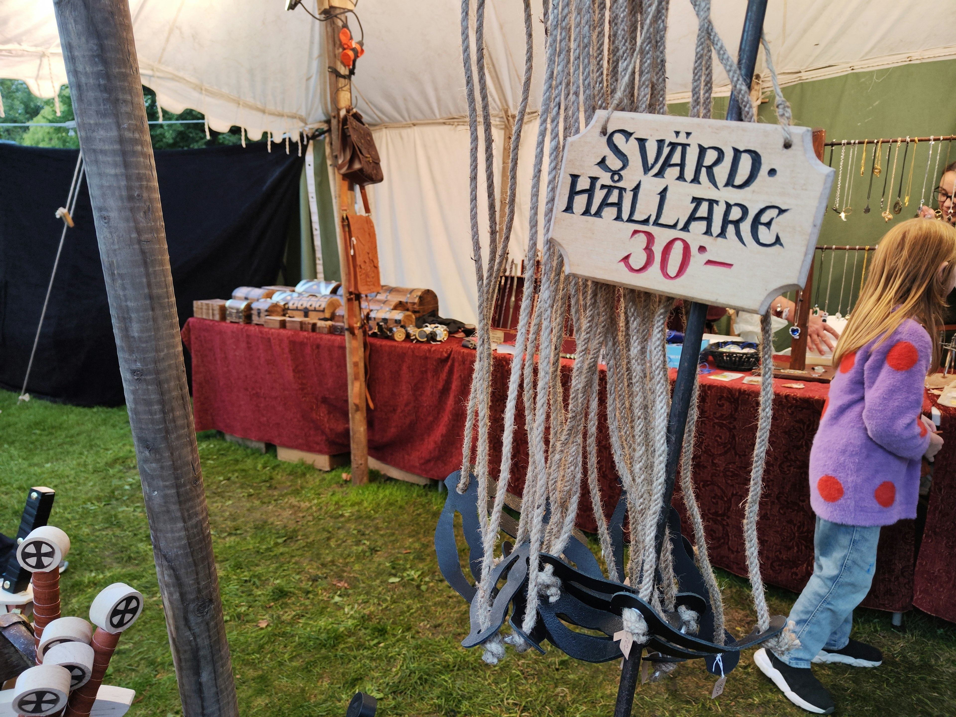 Market scene inside a tent with a sign for Svärd-Hallare and a child present