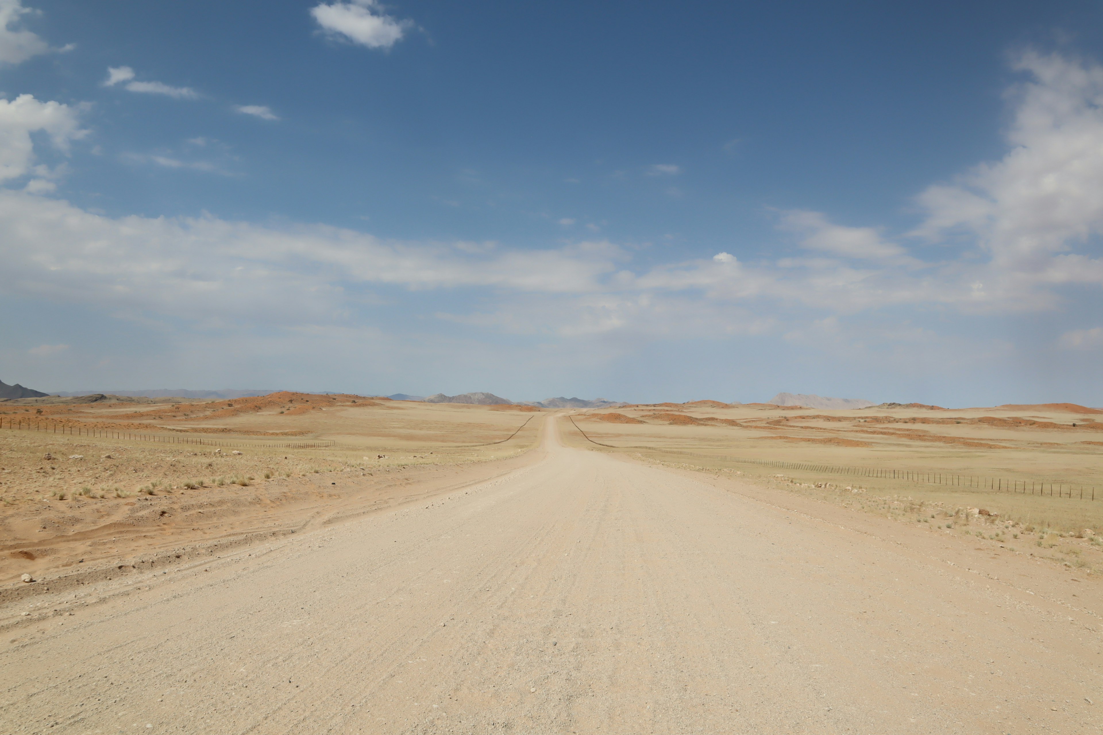 Strada sterrata che si estende attraverso un paesaggio secco sotto un cielo azzurro