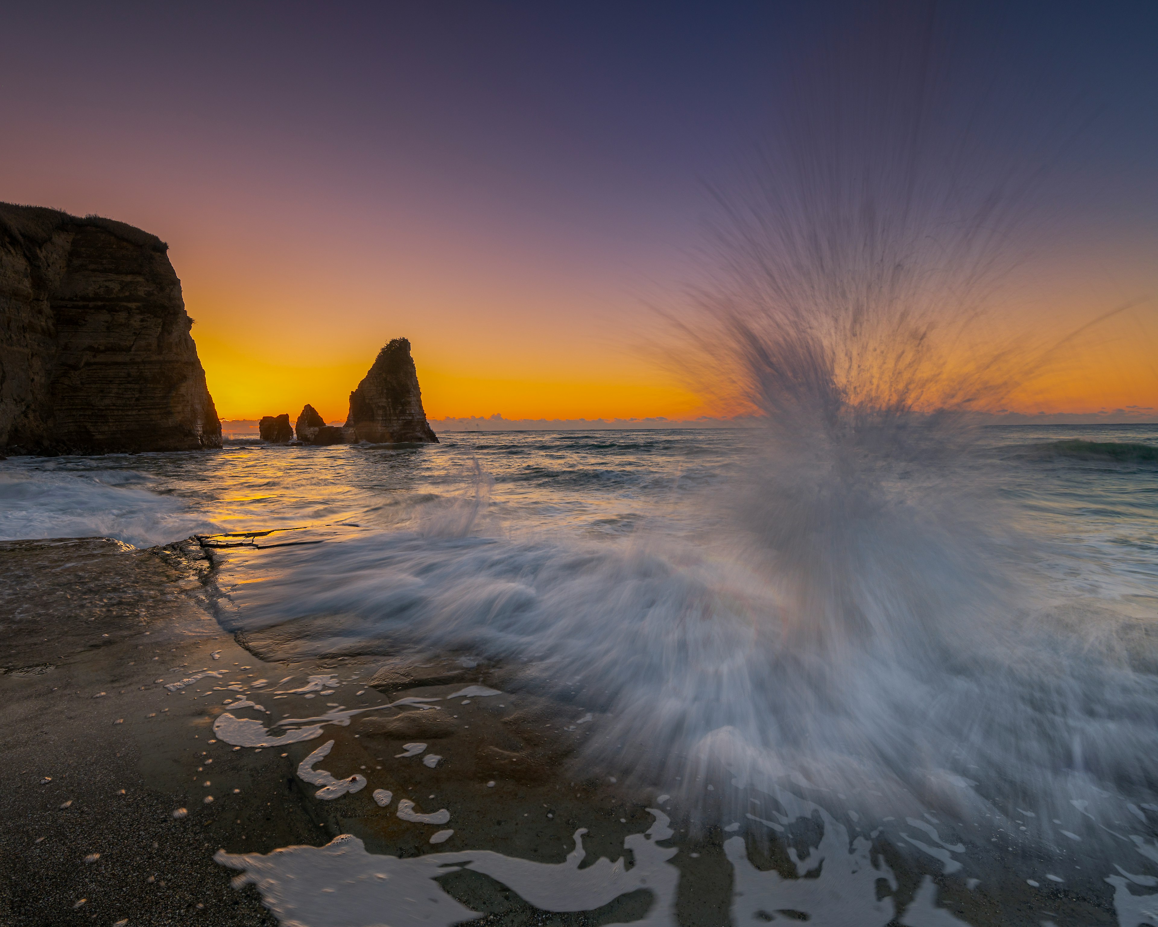 Atardecer costero con rocas y olas salpicando