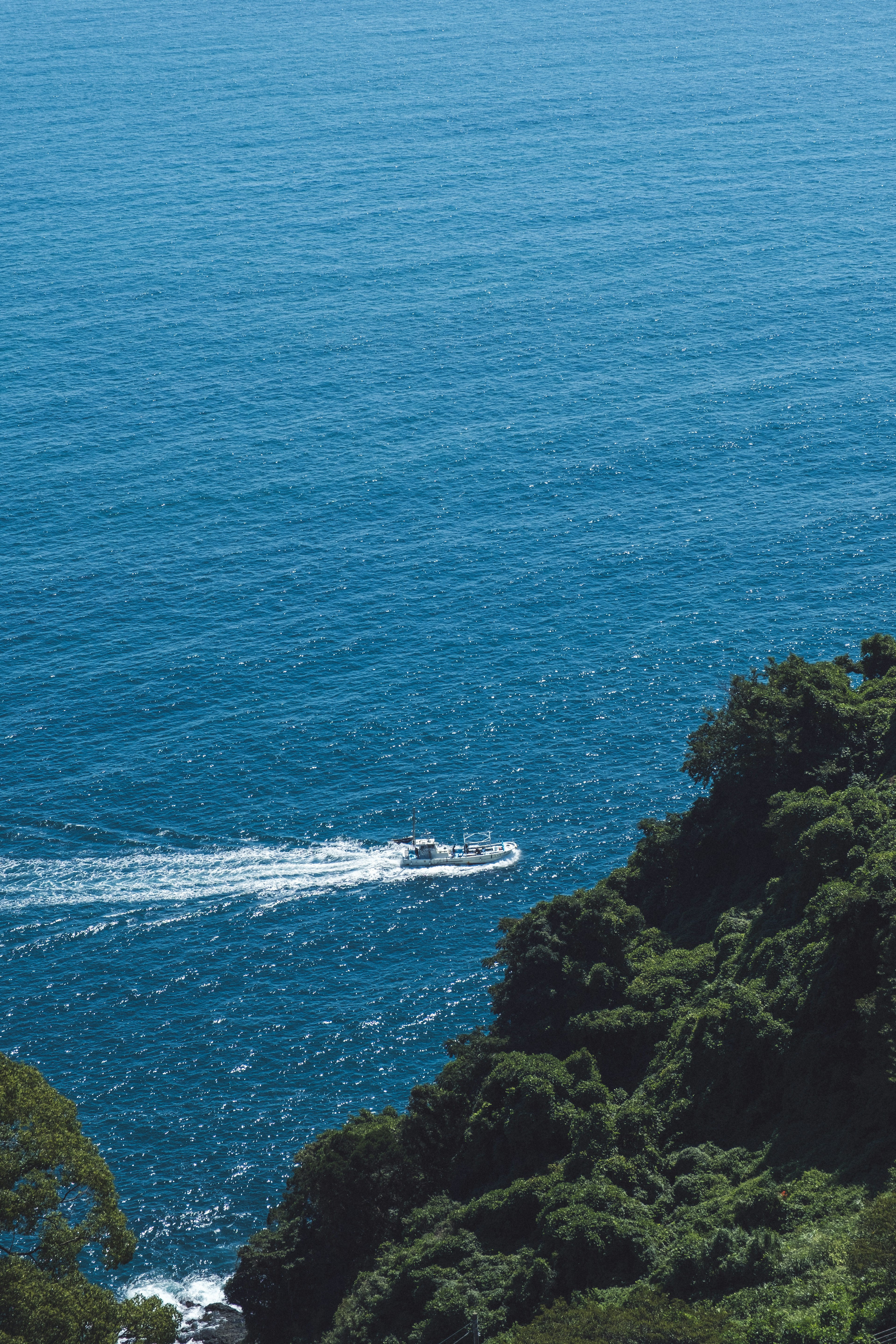 A boat navigating the blue sea with green hills in the background