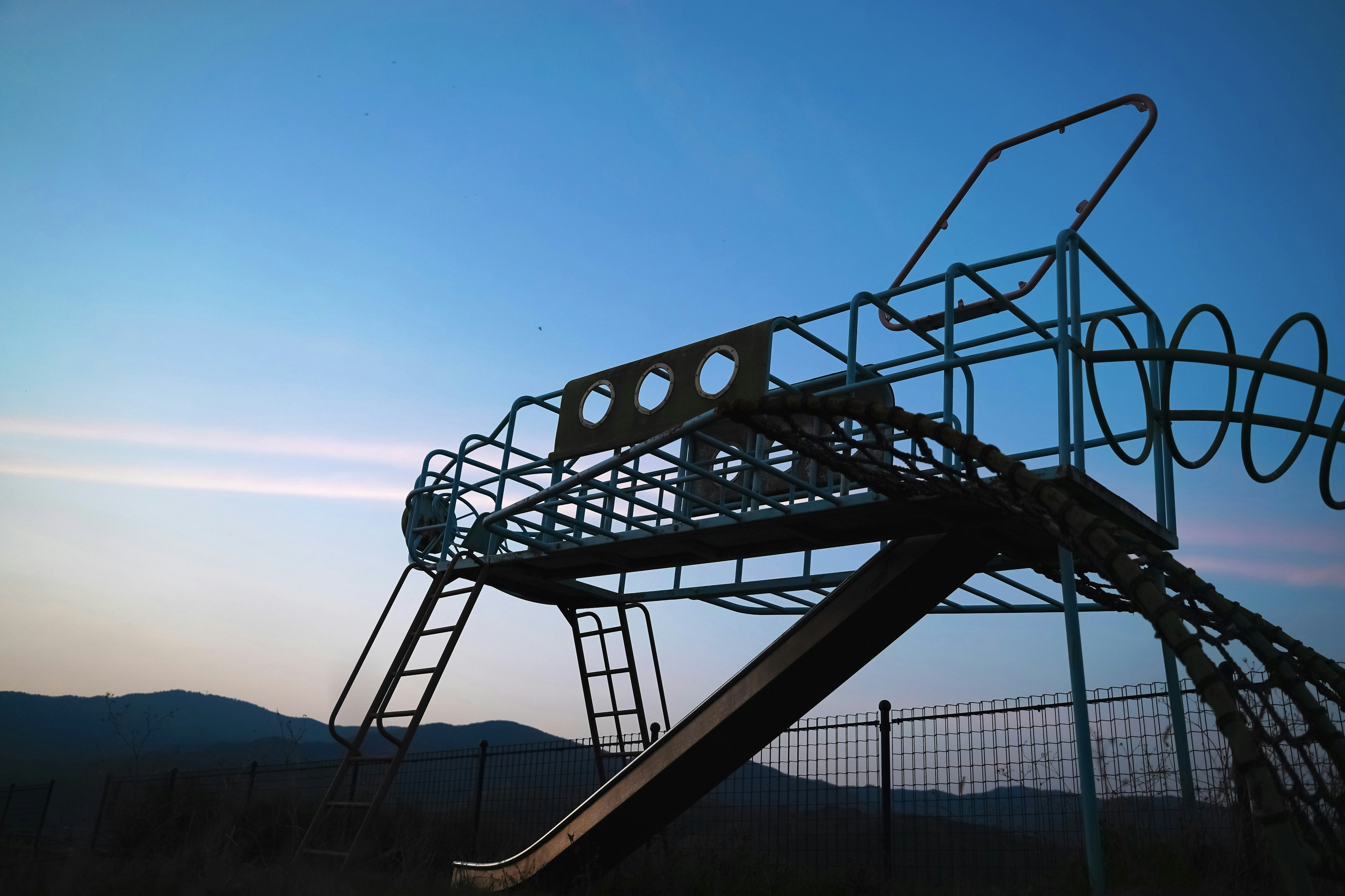 Playground slide and ladder silhouetted against a sunset sky