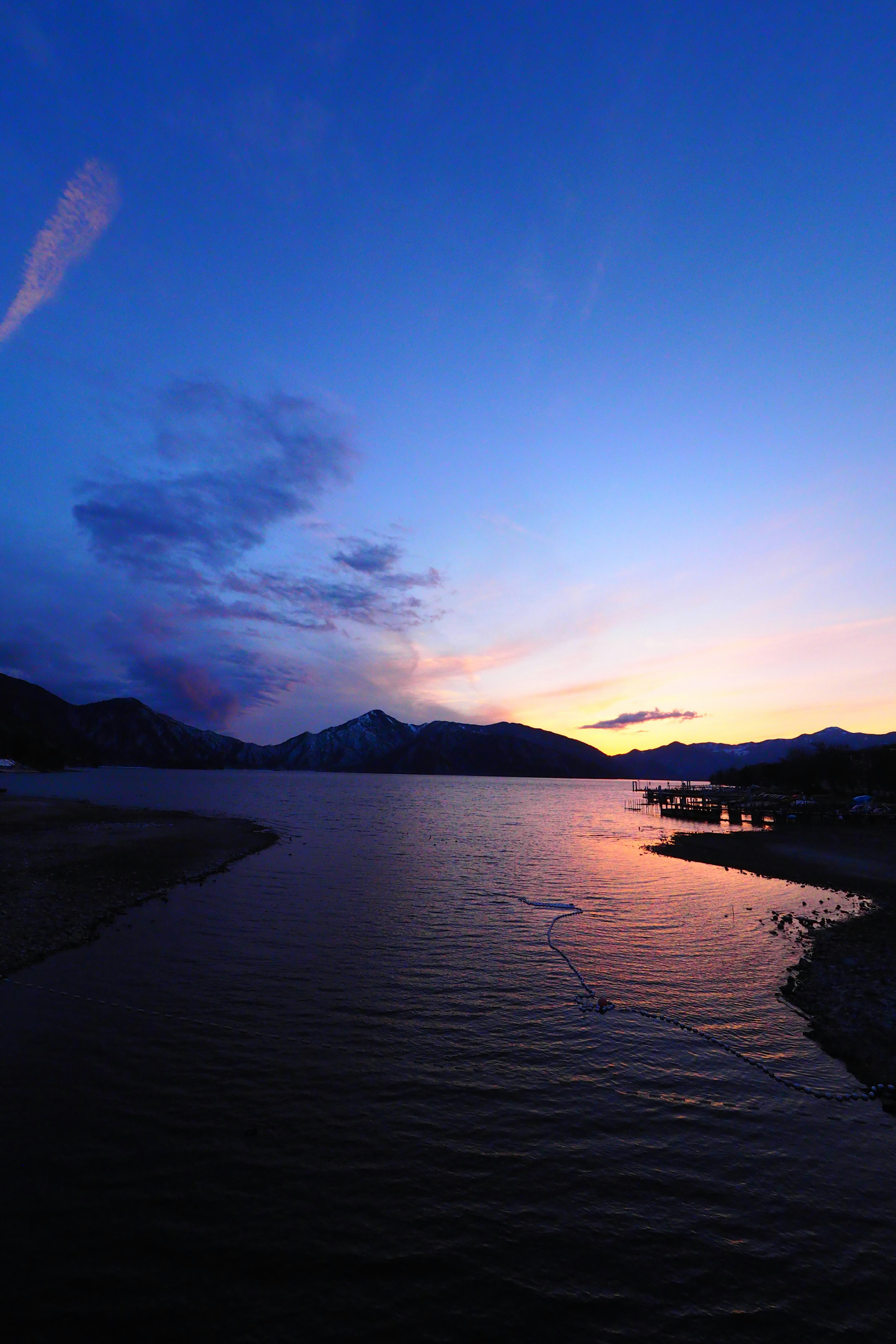 Malerscher Sonnenuntergang über einem See mit Reflektionen von Bergen und buntem Himmel