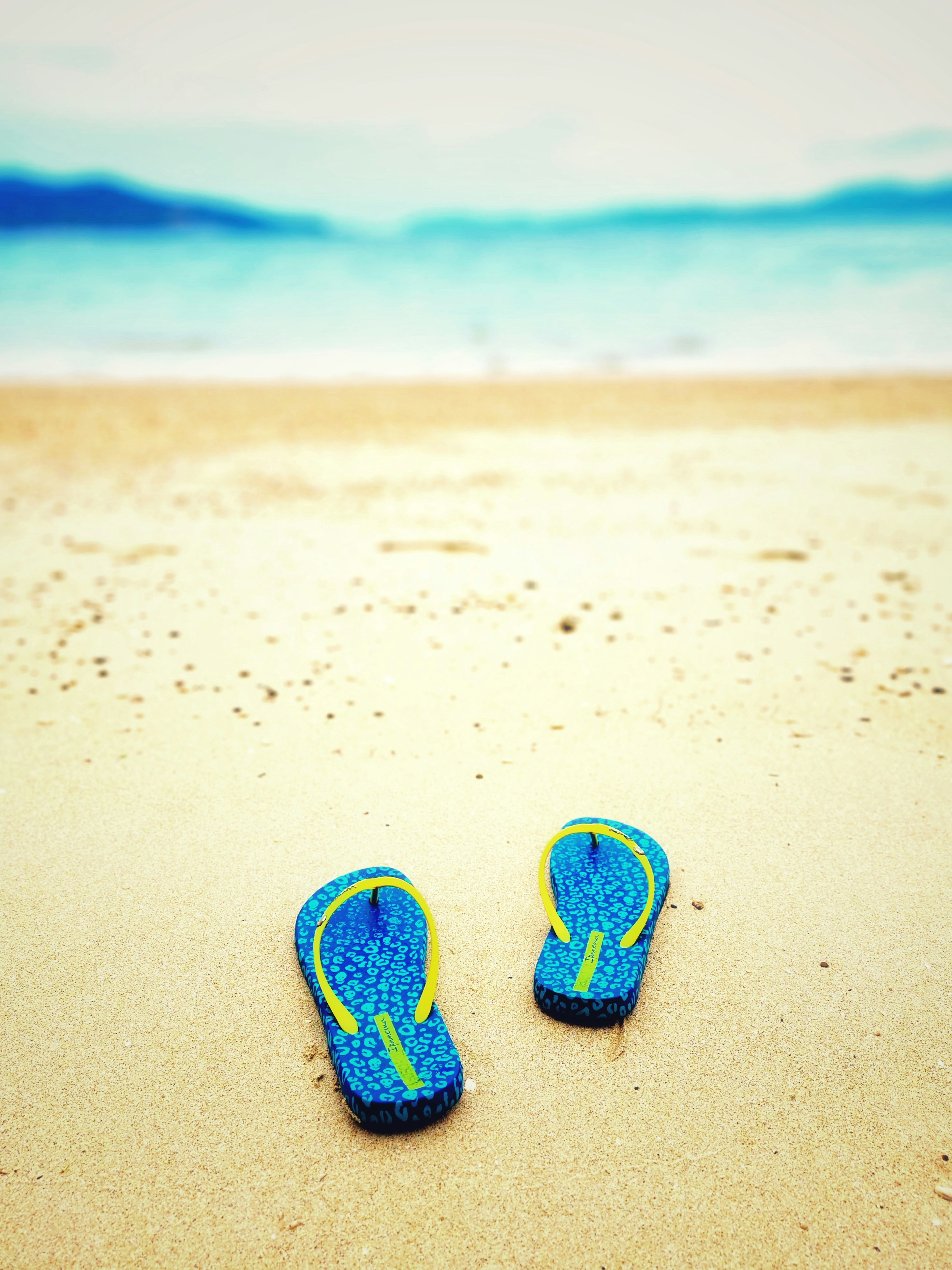 Blue flip flops on a sandy beach with ocean in the background