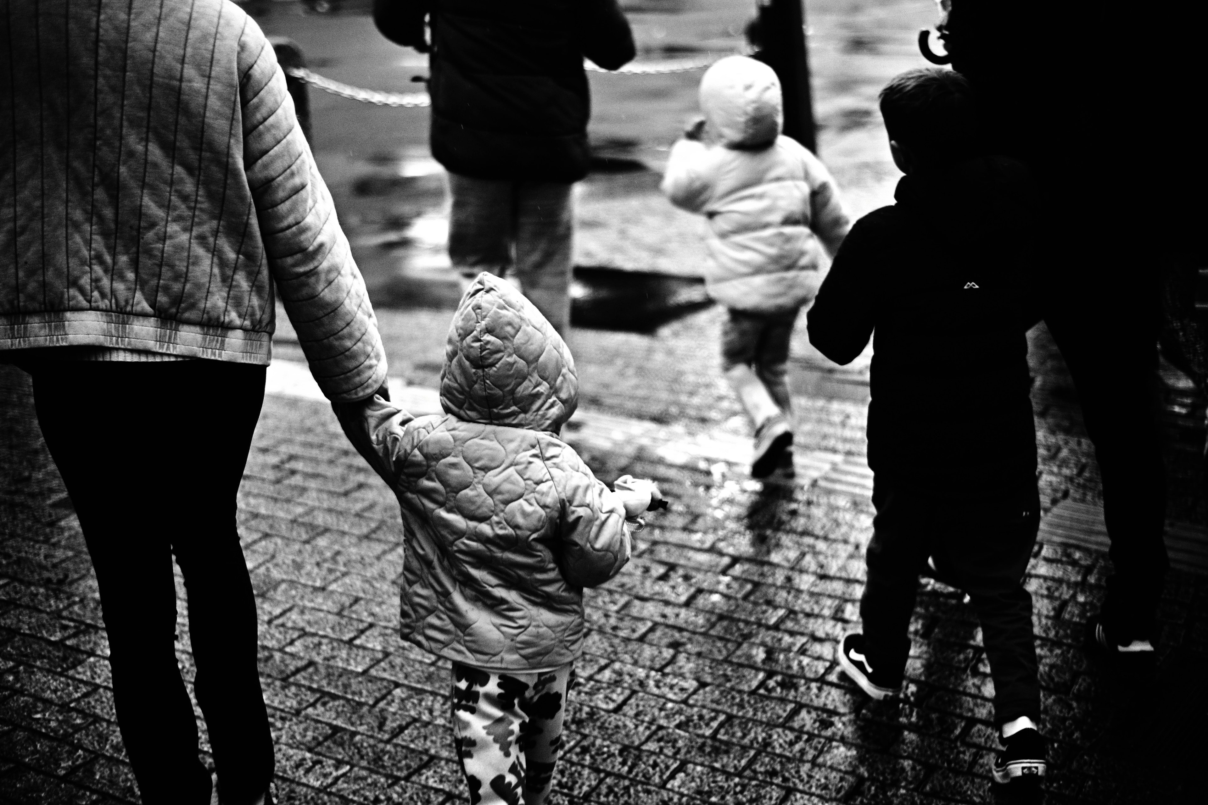 Un parent tenant la main d'un enfant marchant dans un décor en noir et blanc